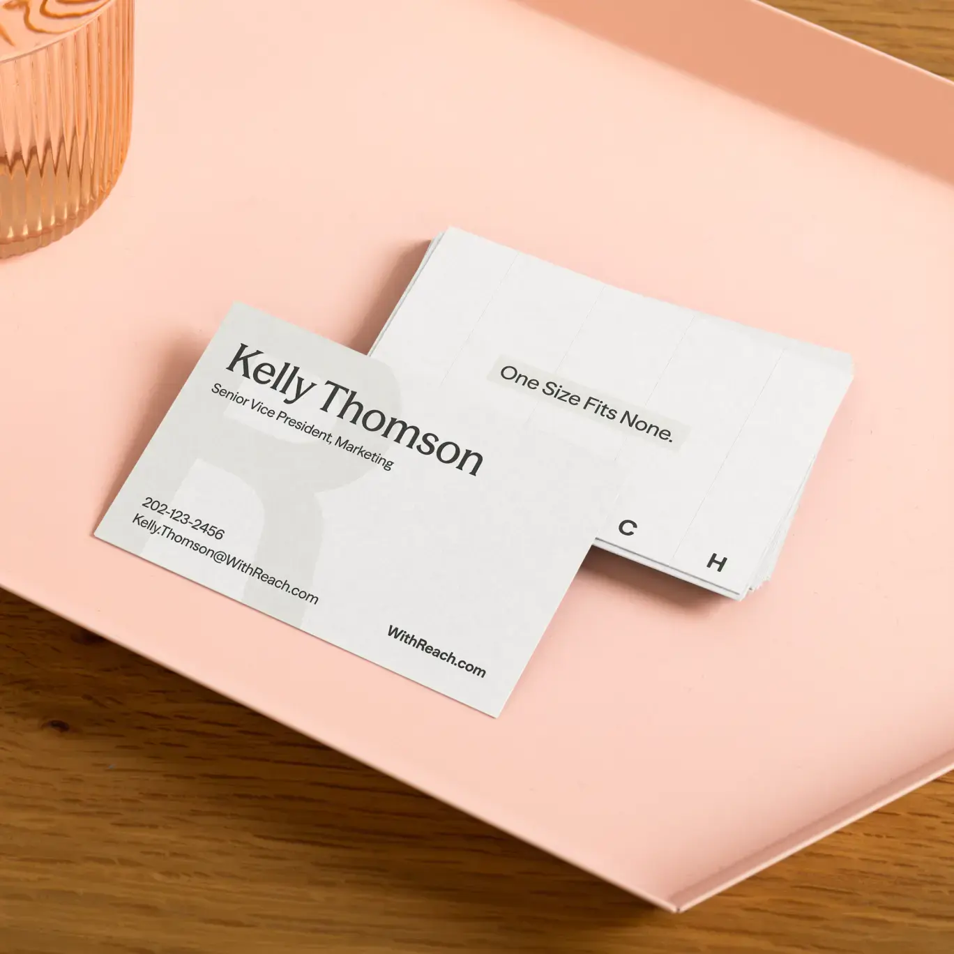 Reach business cards on a peach tray, combining serif names, subtle grid lines, and the tagline “One Size Fits None.”