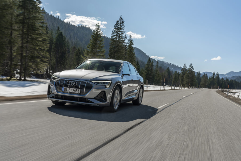 Photo of an Audi driving on a road with trees and mountains in the background