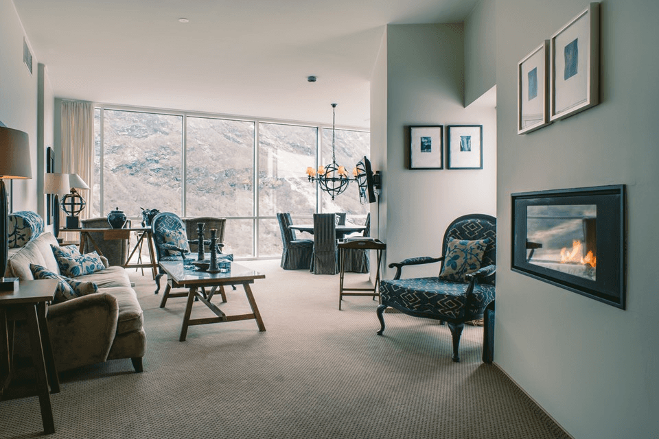 A spacious and elegantly decorated living room features cozy seating, a modern fireplace, large windows with scenic mountain views, and a stylish dining area, enhancing the ambiance of relaxation and comfort.