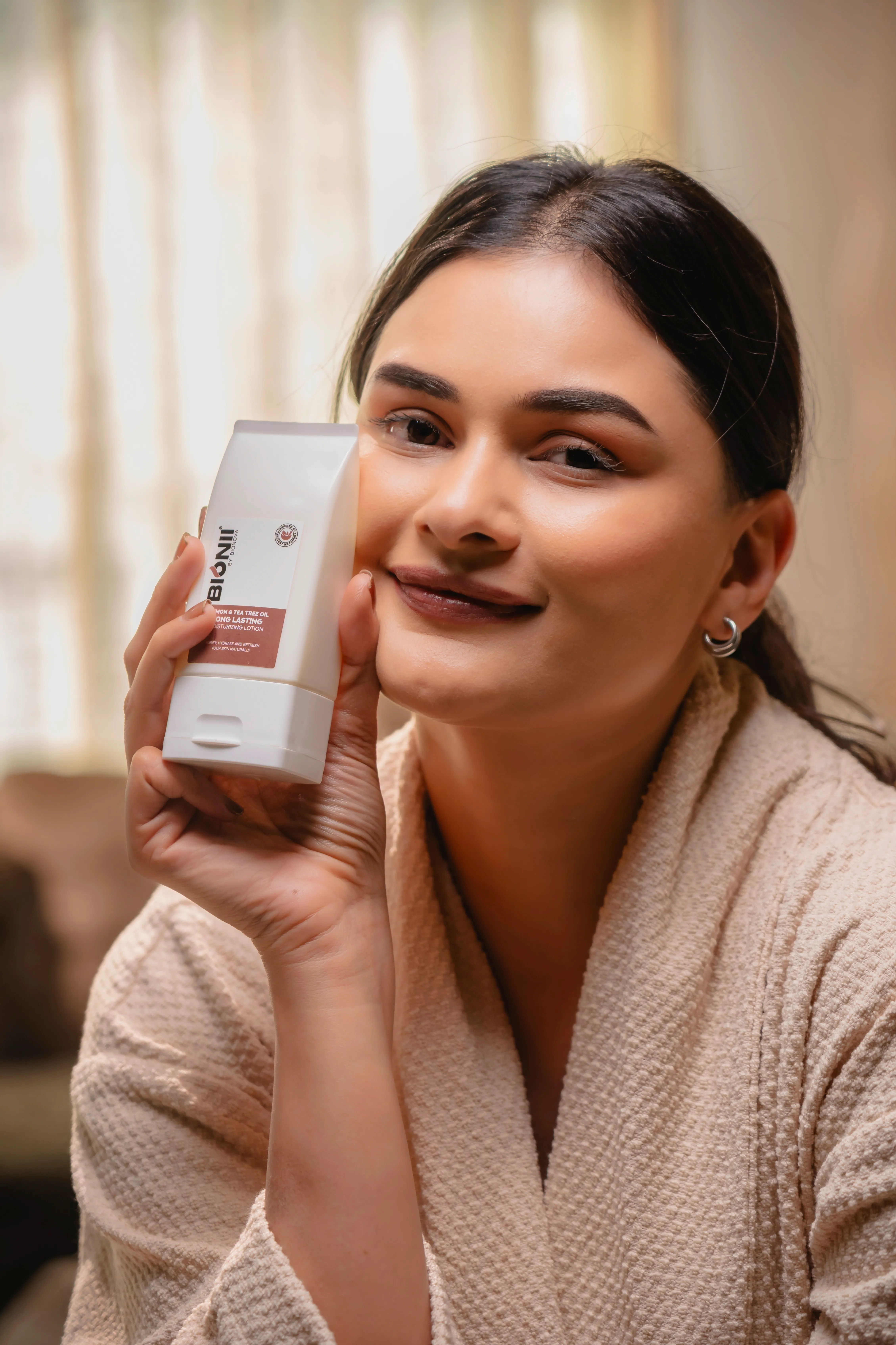 A smiling woman in a bathrobe holds up a can of beverage, with soft natural light and a cozy background.