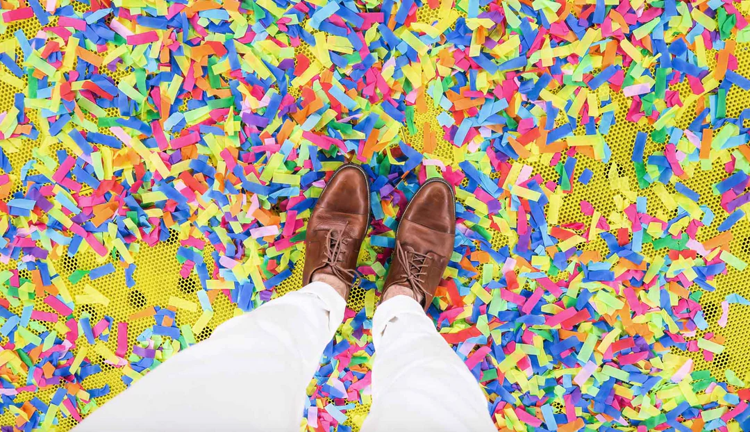person with brown dress shoes standing on rainbow confetti