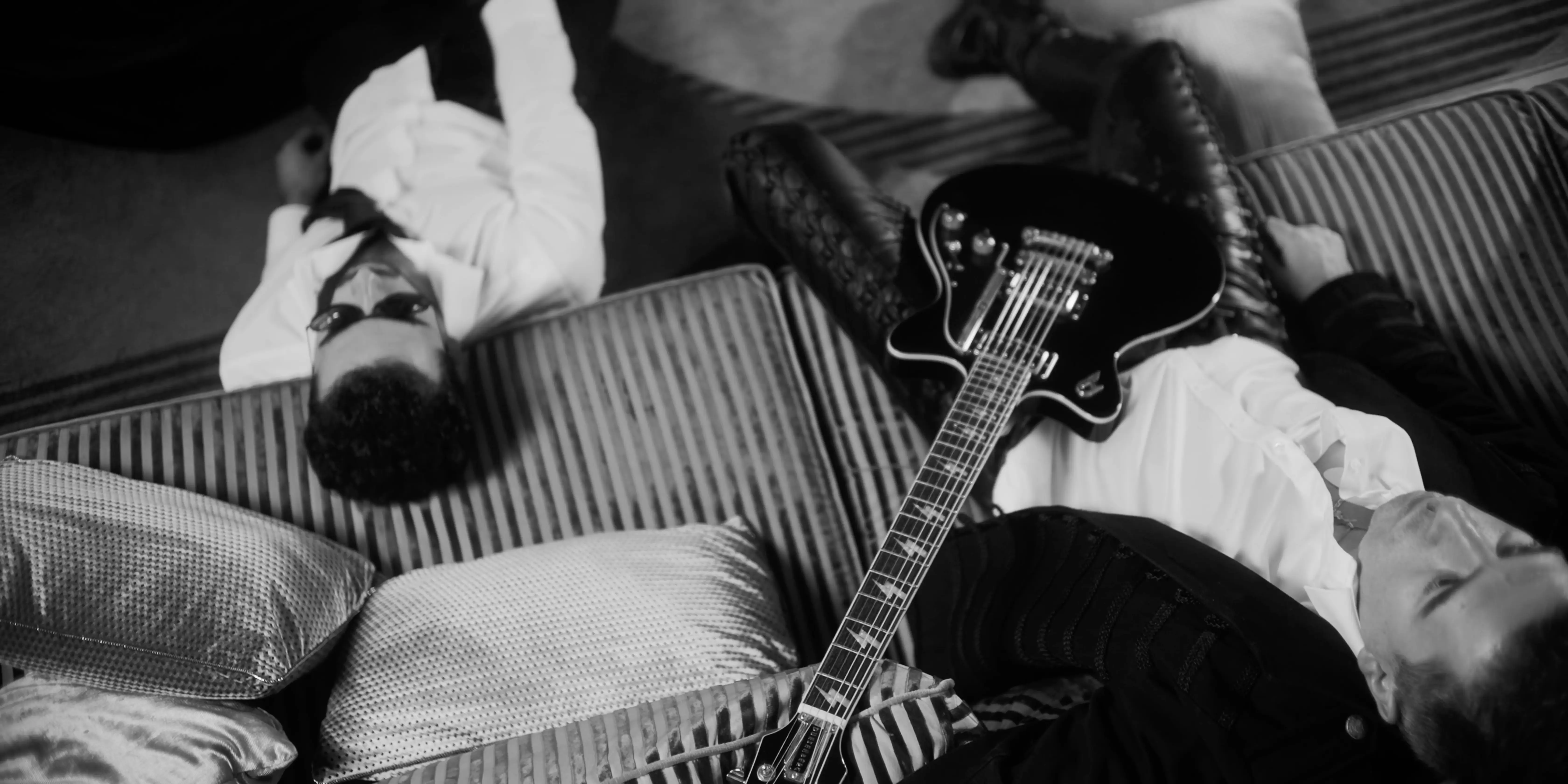 A person lies on a surface, surrounded by clothing and items, captured in black and white.