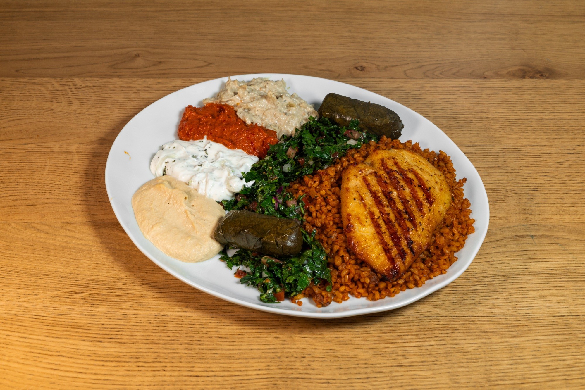 Tallrik med grillad kyckling, bulgur, tabbouleh, hummus, muhammara, tzatziki och vinbladsdolmar.