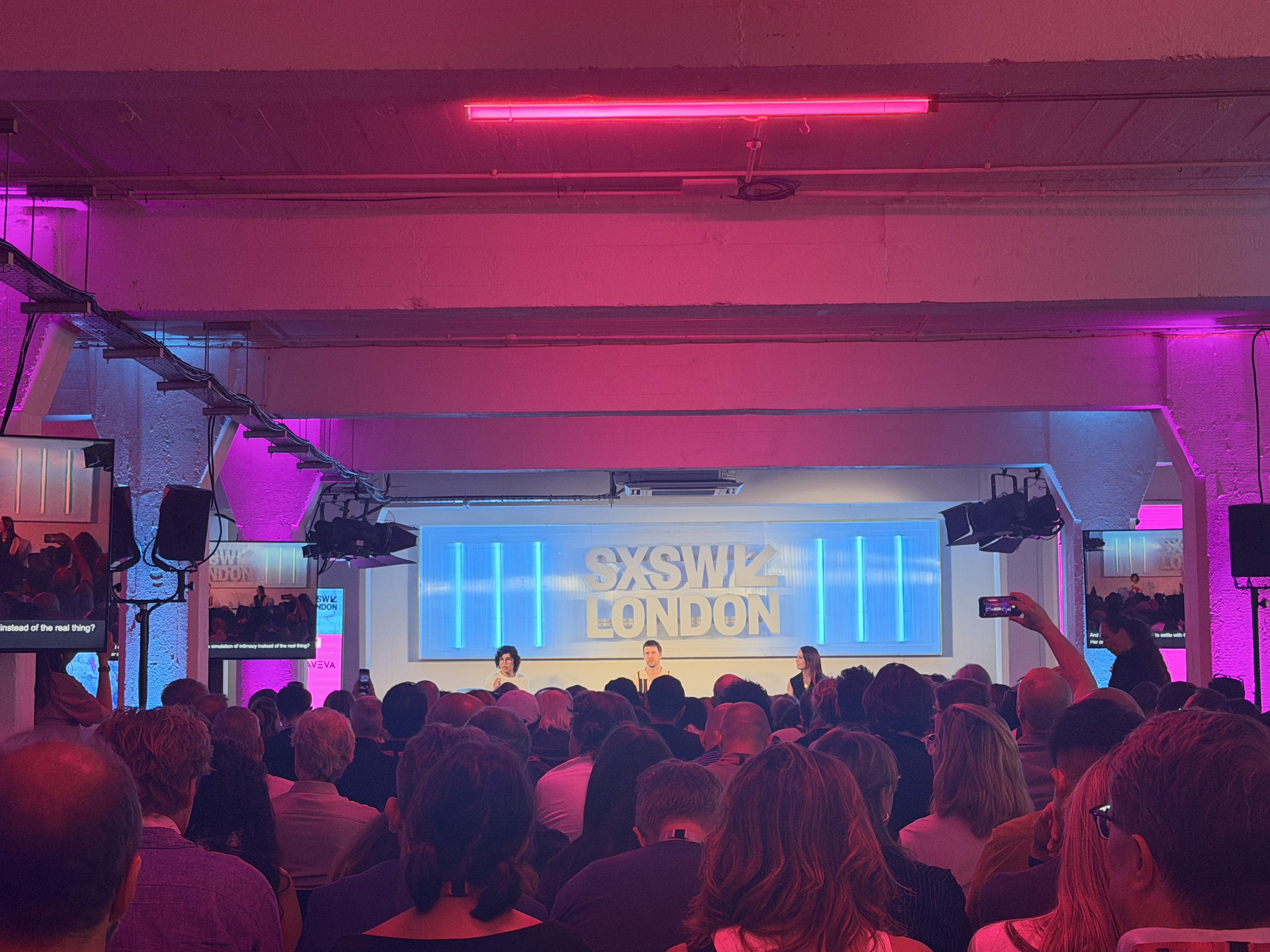 Image shows SXSW logo on a stage screen, in a room of people seated.