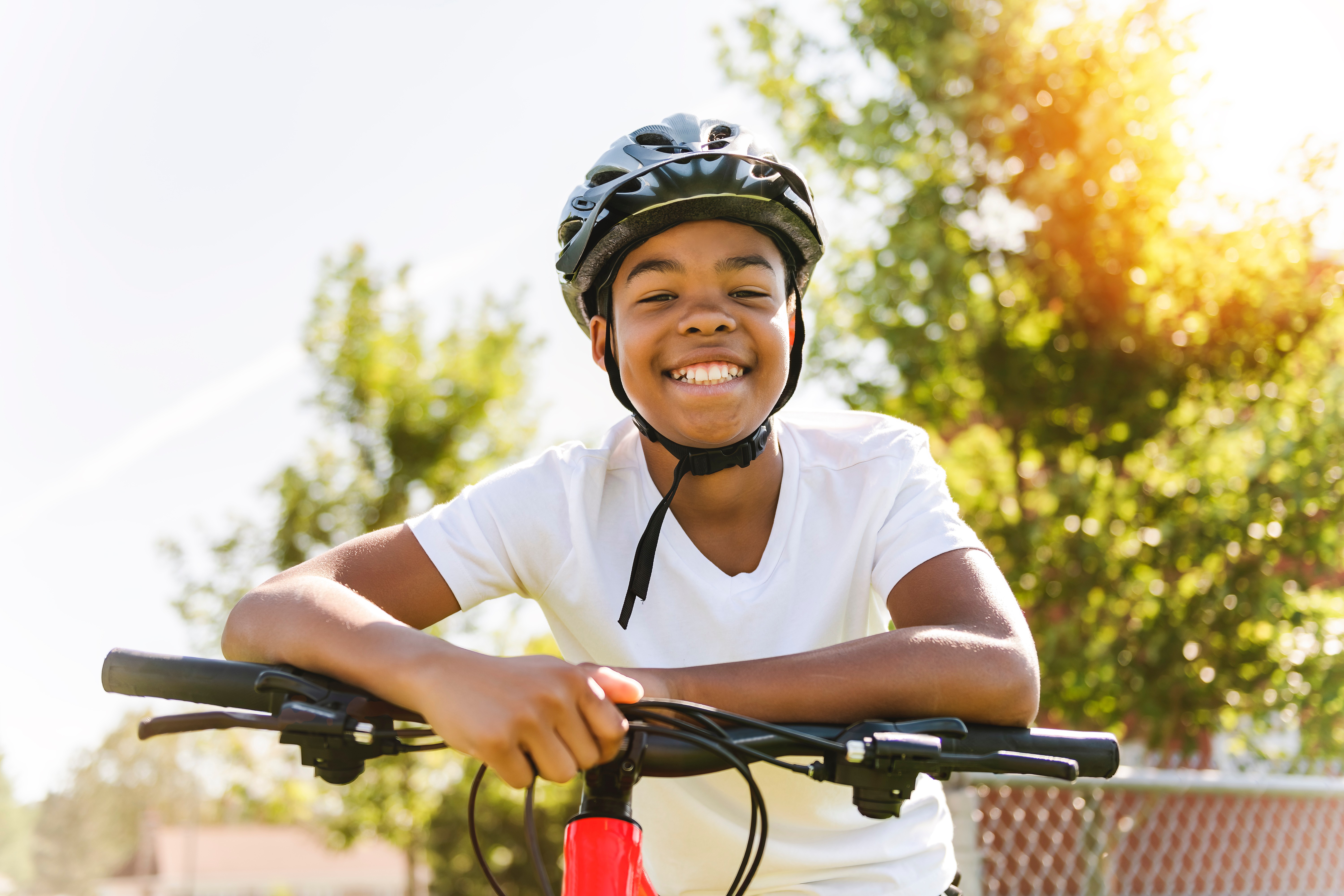 Smiling boy wearing a cycle helmet leaning on his bike handlebars outdoors