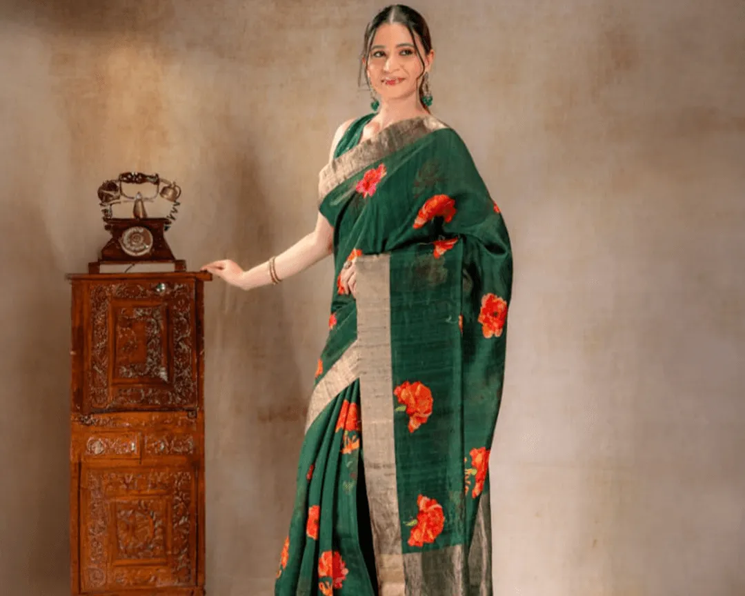 A woman wearing a green Dupion silk saree from That Saree Shop, featuring elegant golden borders and delicate orange floral prints, blending textured luxury with vibrant handcrafted detail.
