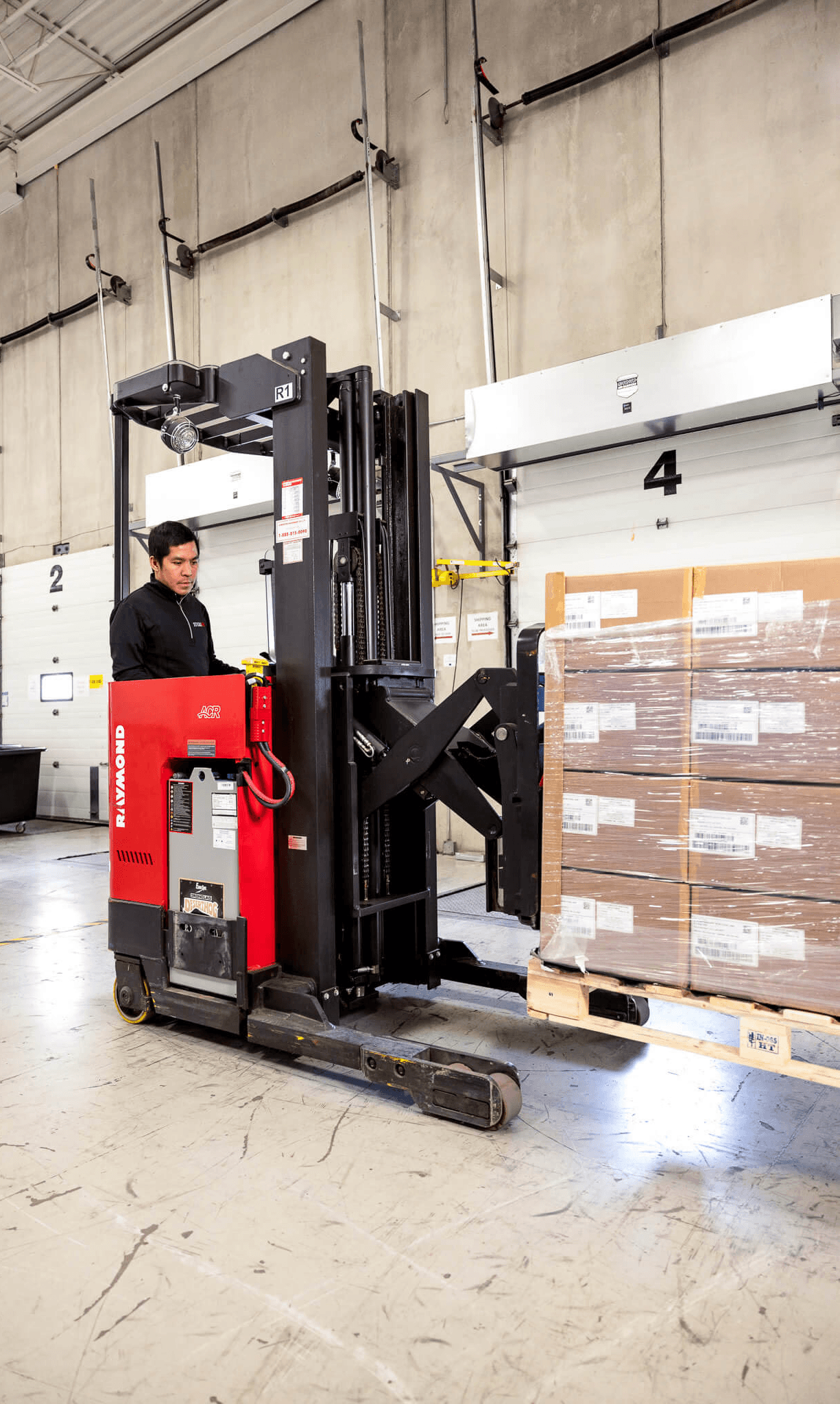 Three SteriMax warehouse team members smiling and collaborating with a clipboard and scanner in a large distribution facility.