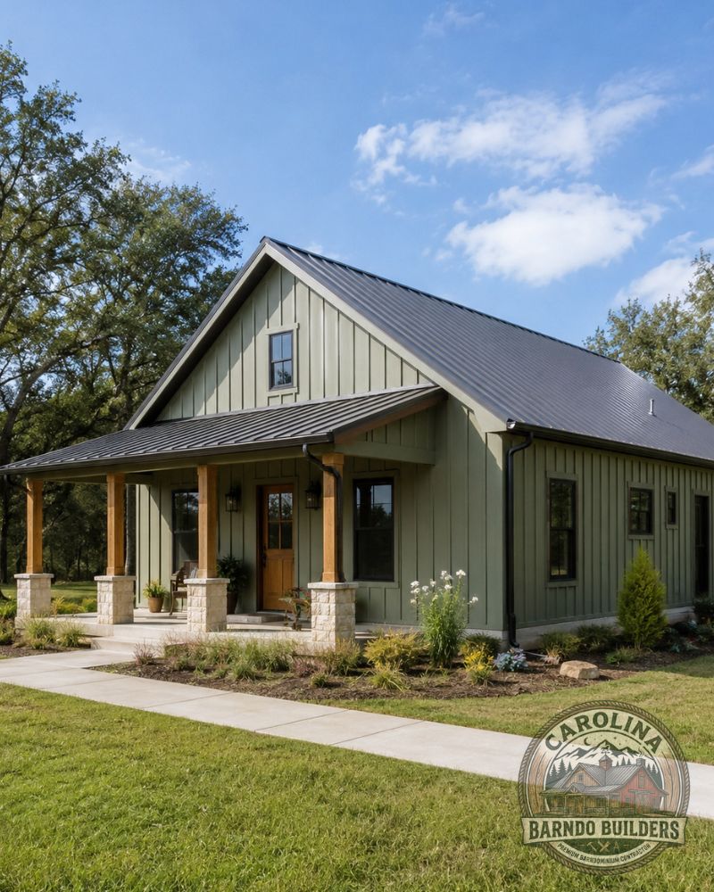 Sage green barndominium home in Davie County NC with black metal roof, covered front porch, timber posts, stone columns, and landscaped walkway.