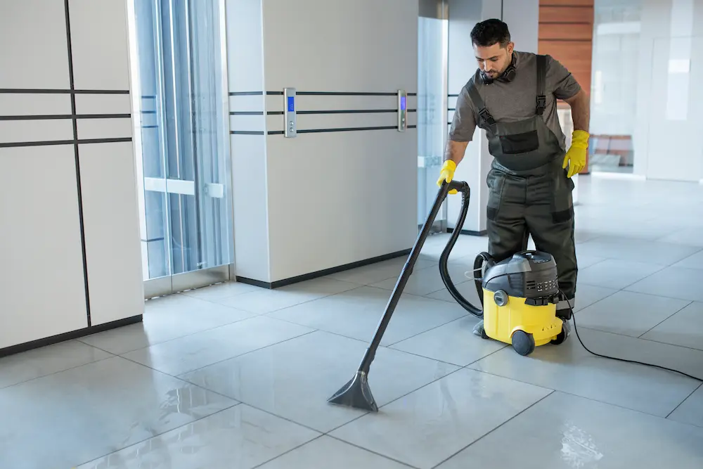 Professional cleaner using yellow carpet extractor to clean tile floor in commercial space after builders