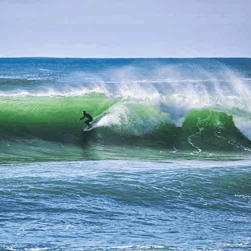 Surfer riding a large green wave – surfboard rental in aljezur.