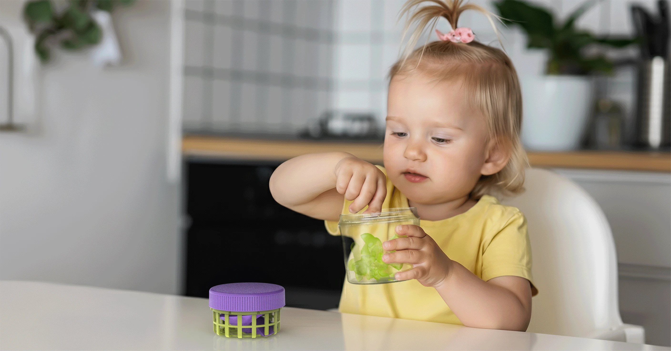 A clear container with a green basket and a purple lid, while the kid are trying to eat a piece of grapes inside of the container