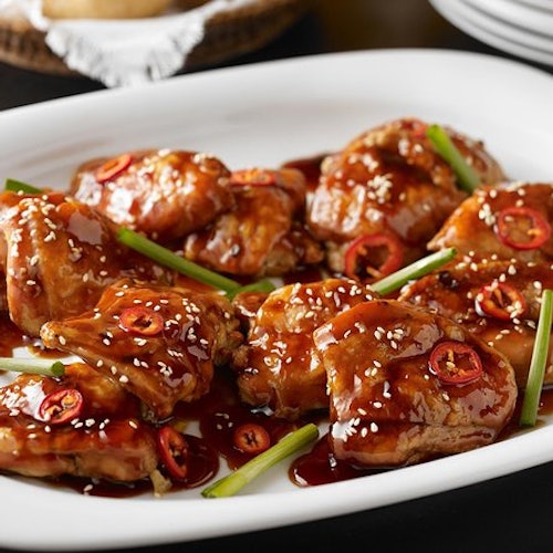 Sliced roast beef covered in a dark gravy, garnished with herbs, on a white rectangular plate