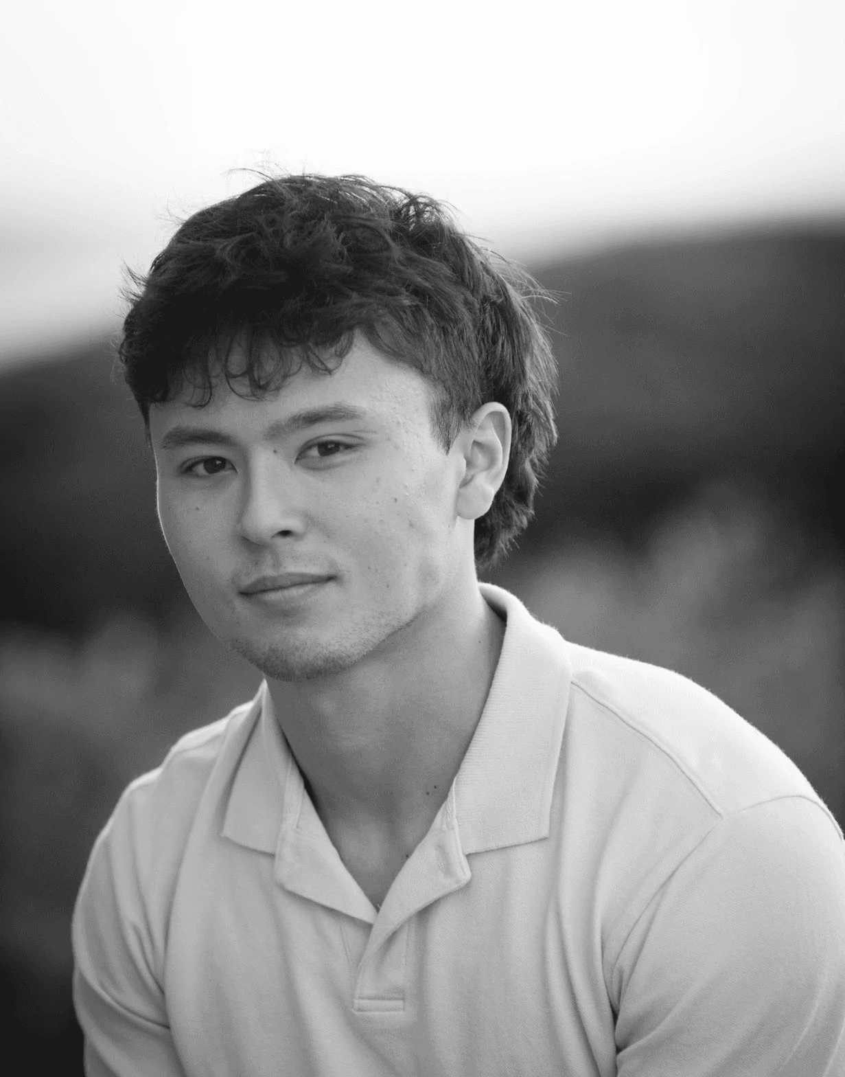 Portrait of a young man with short hair, wearing a dark t-shirt, against a plain background.