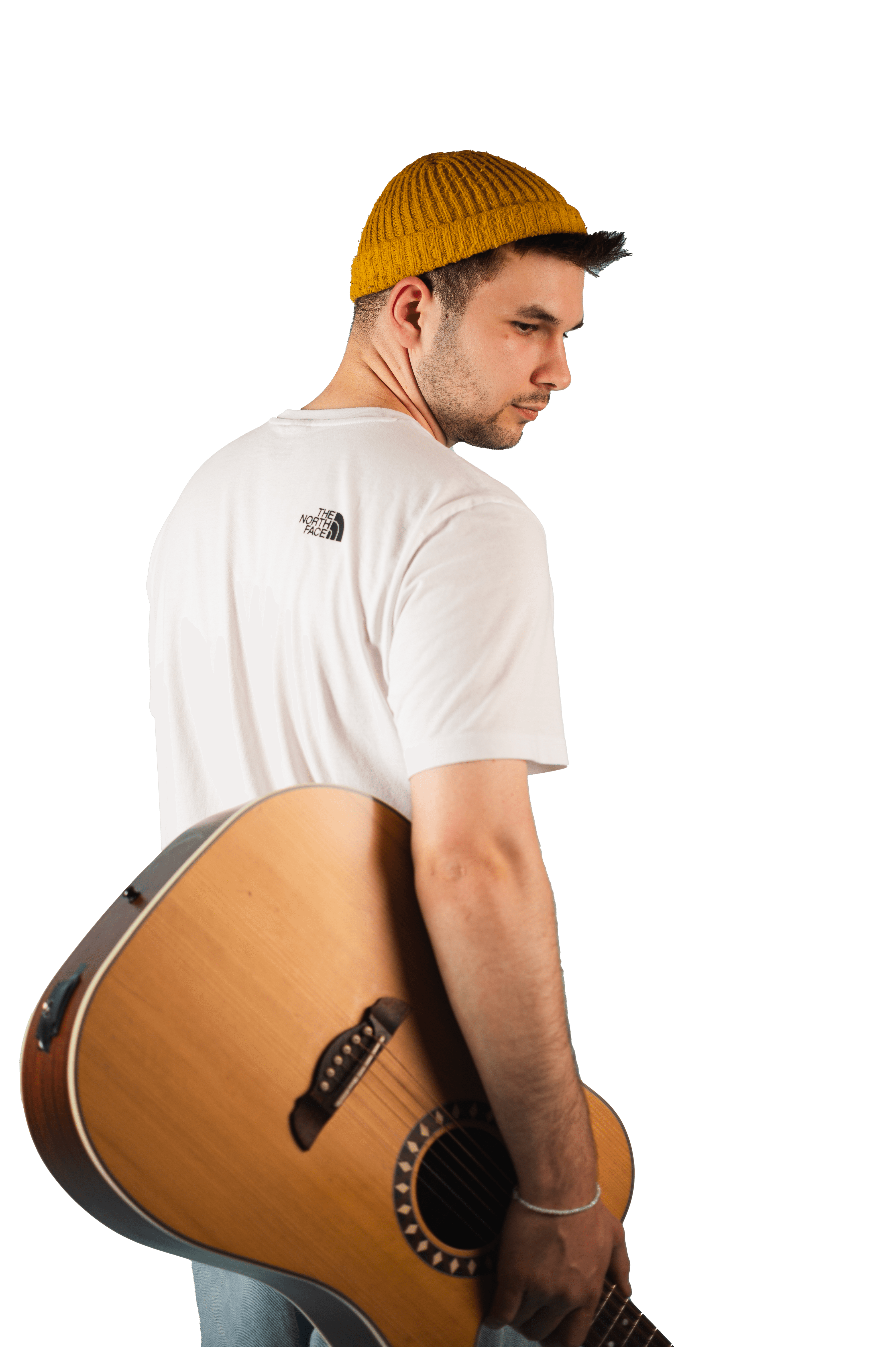 Ein junger Musiker mit einer gelben Mütze und einem weißen T-Shirt, der eine Akustikgitarre über der Schulter trägt und zurückblickt.