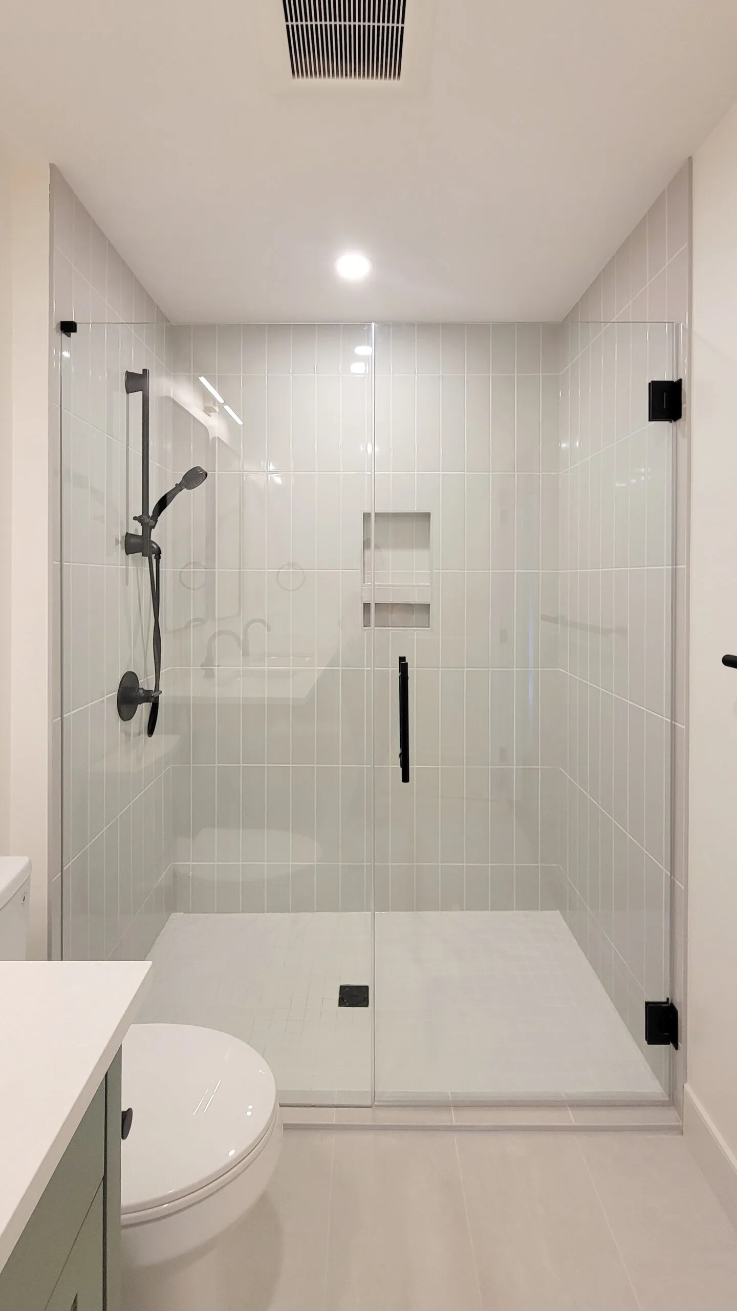 Image of walk in large shower with vertically stacked light grey subway tiles.