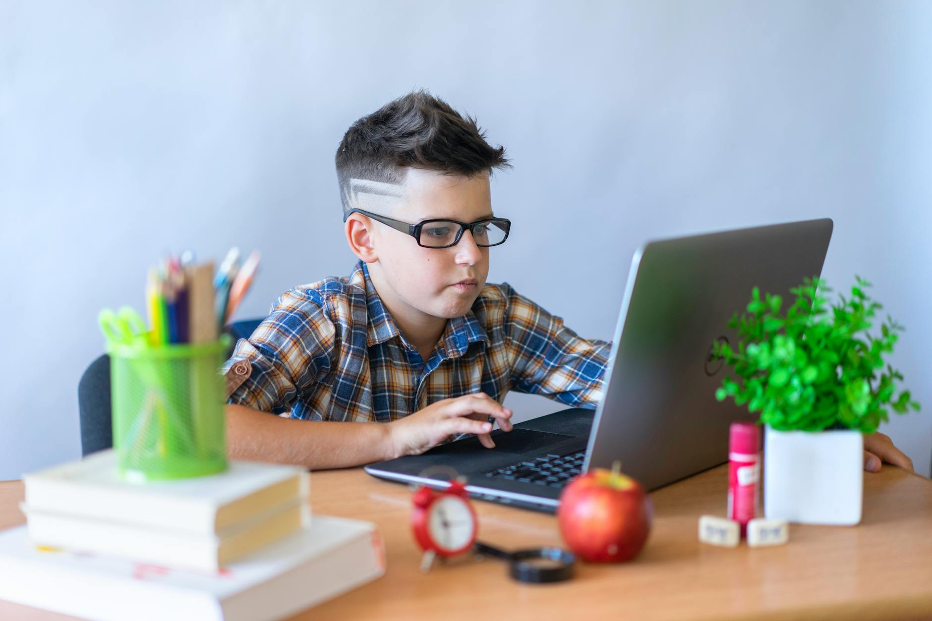 A focused teenager sits at a laptop late at night using student websites to research a history paper.