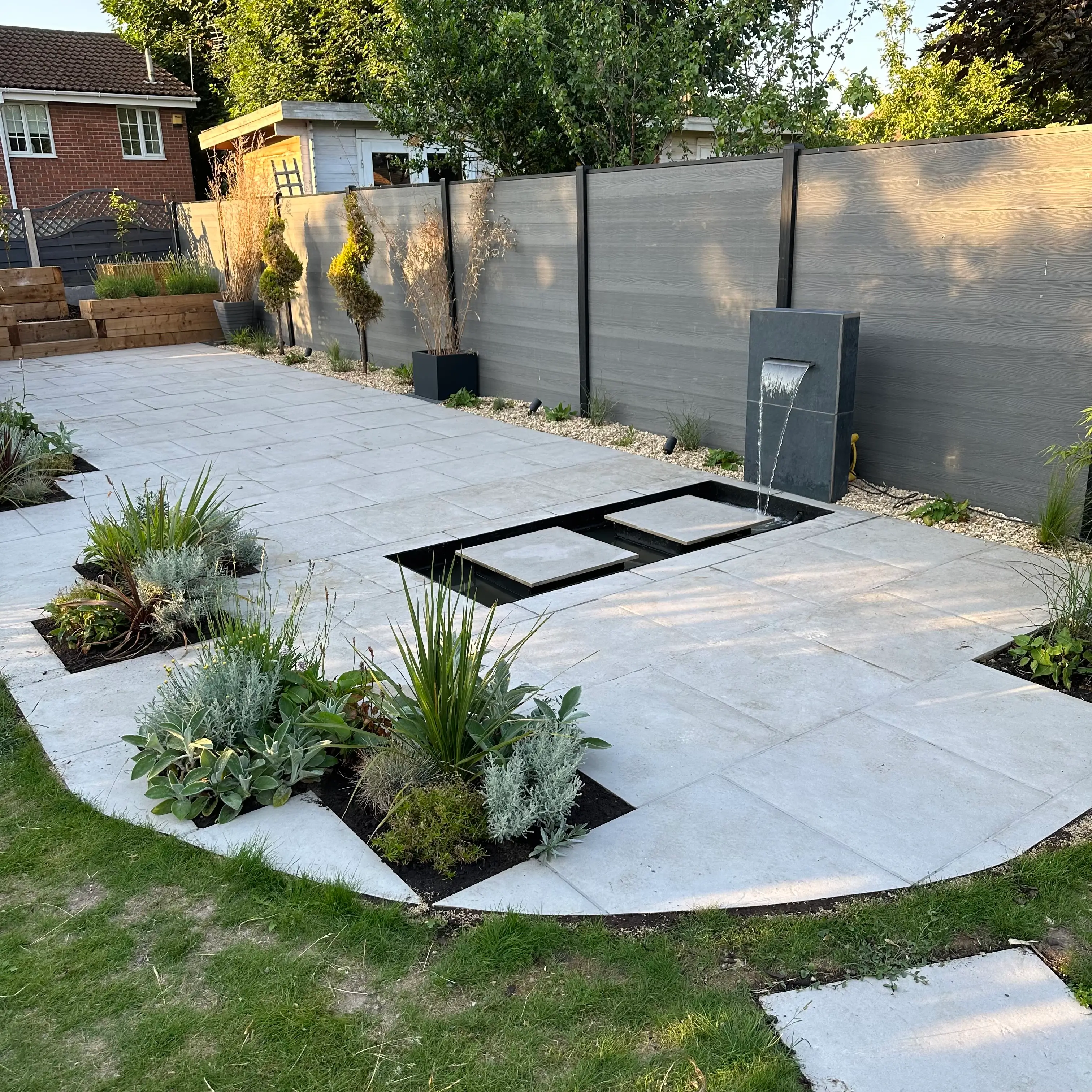 A landscaped outdoor area with a concrete patio, plants, and a shed in the background.