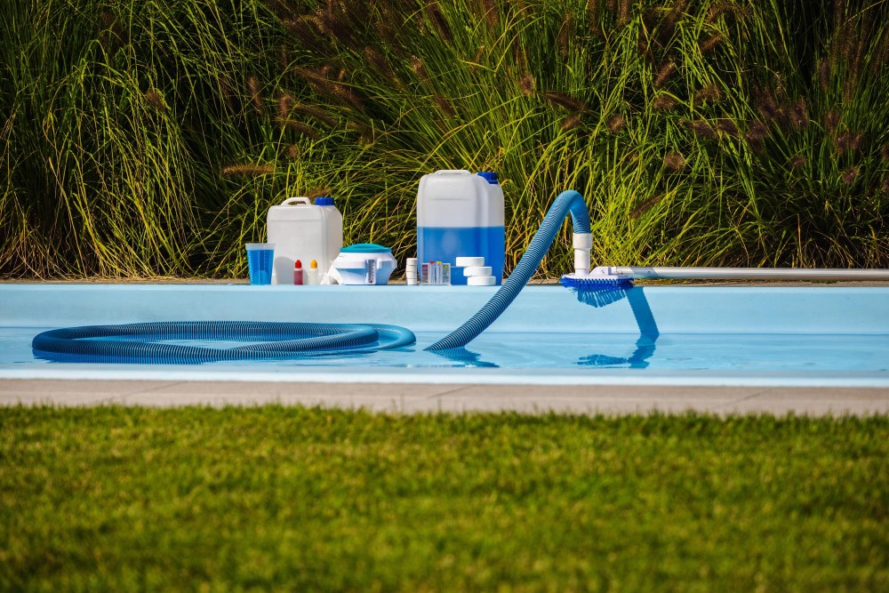 Poolside equipment including pumps, hoses, and chemical containers arranged on the grass.