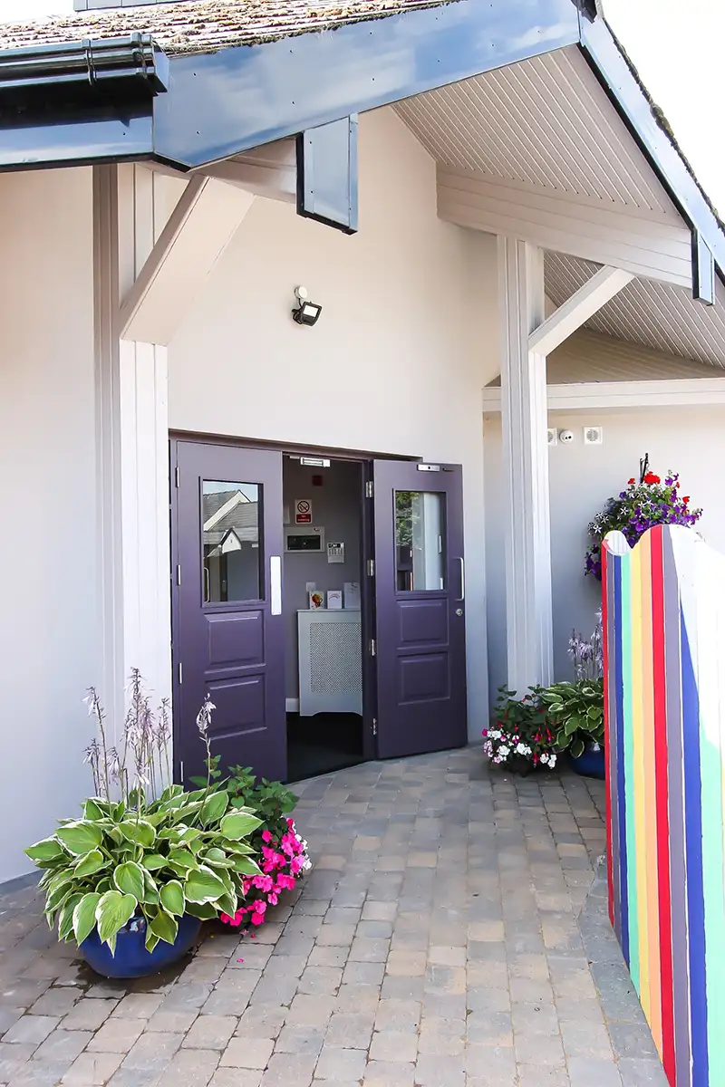 Purple double doors open to a building entrance, with colorful flower pots and rainbow decor.