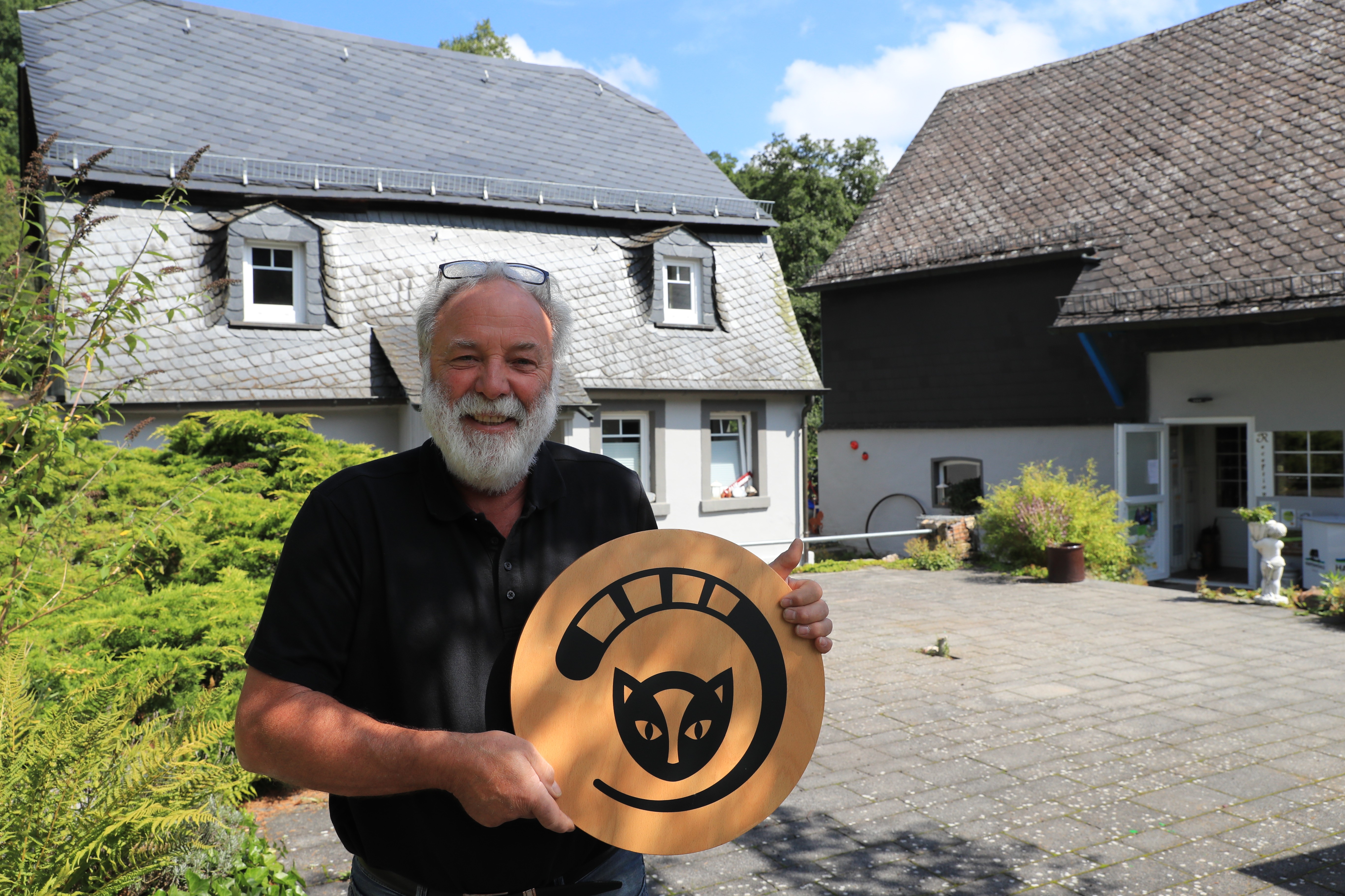 Dieter mit vor der Rezeption mit den Logo Keltenkatze vom Nationlaprk Hunsrück-Hochwald auf einem Holzschild