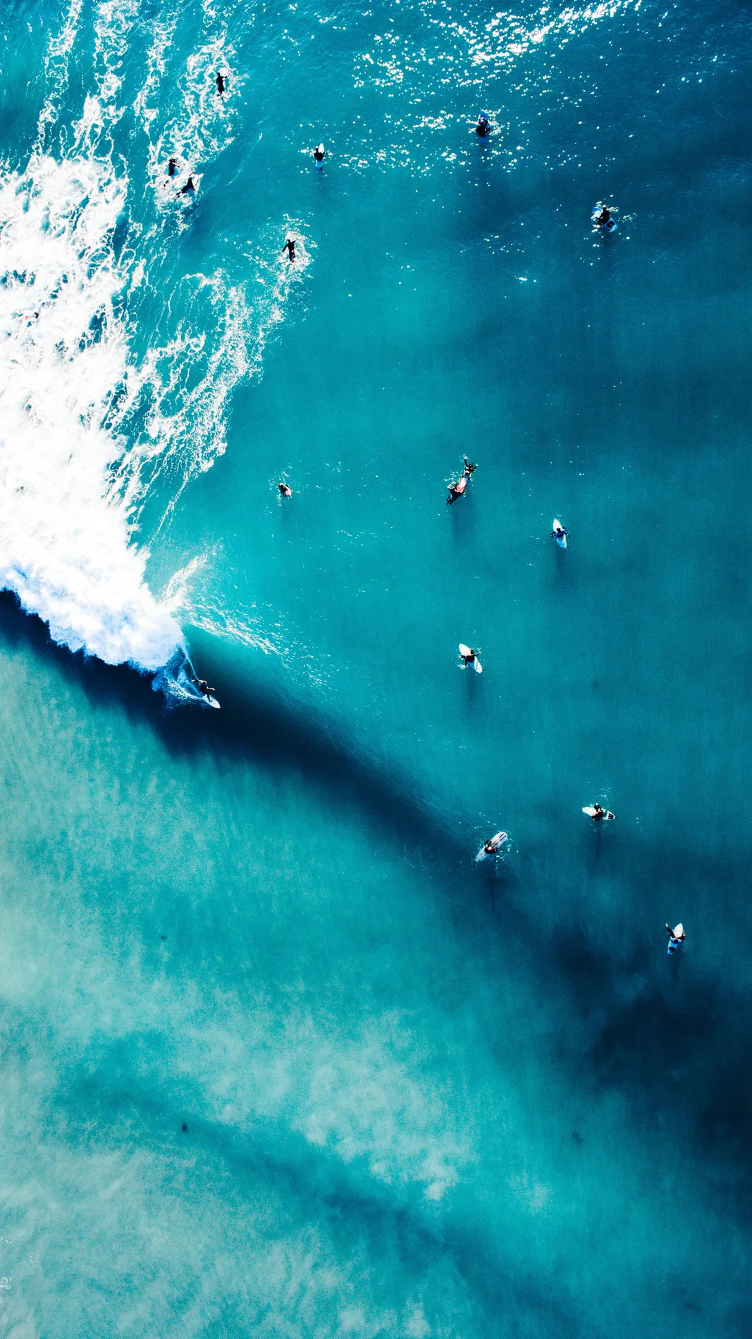 Aerial looking straight down on surfers in turquoise water as a wave breaks