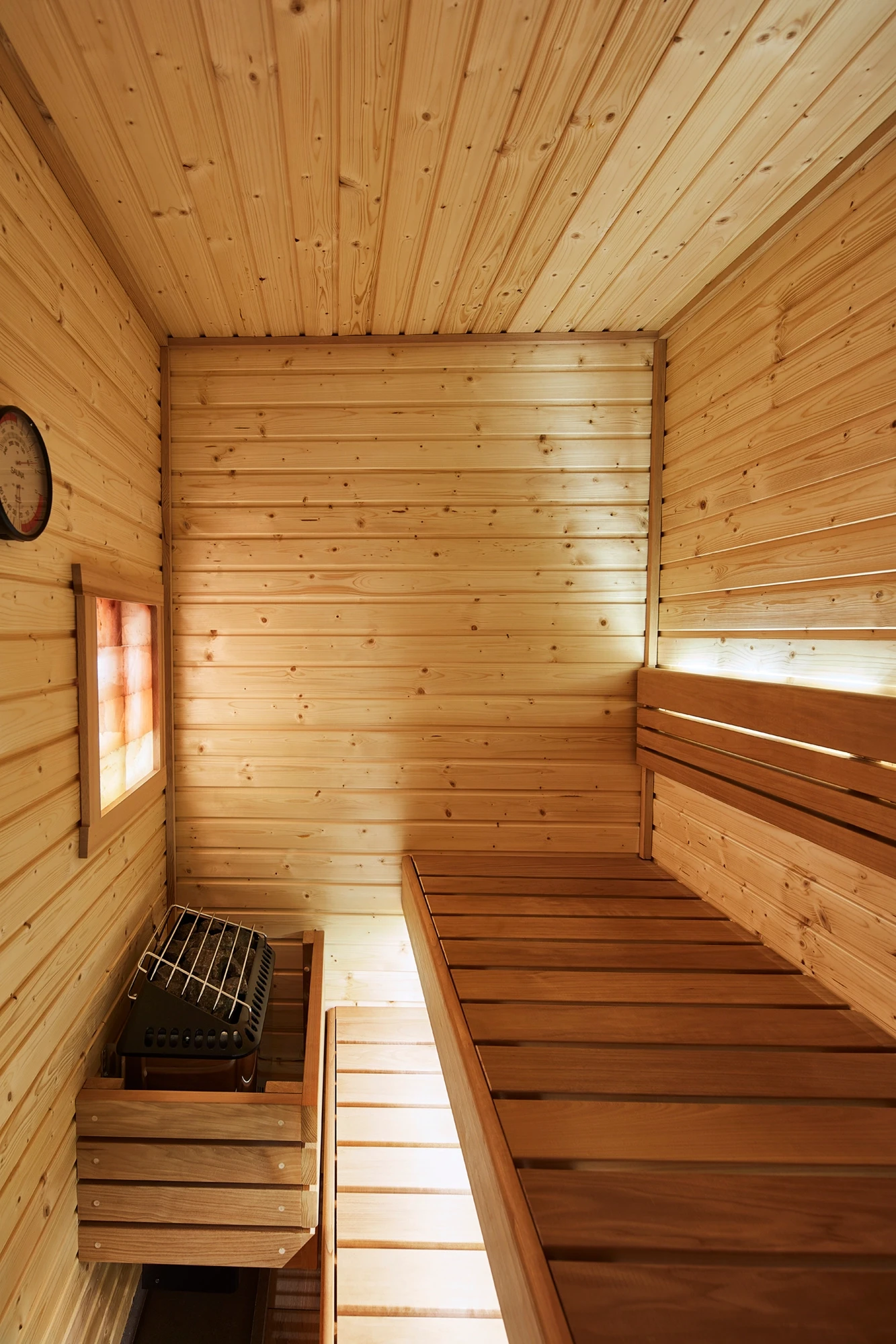 Compact wood-lined sauna with a raised bench, wall thermometer and guarded heater.