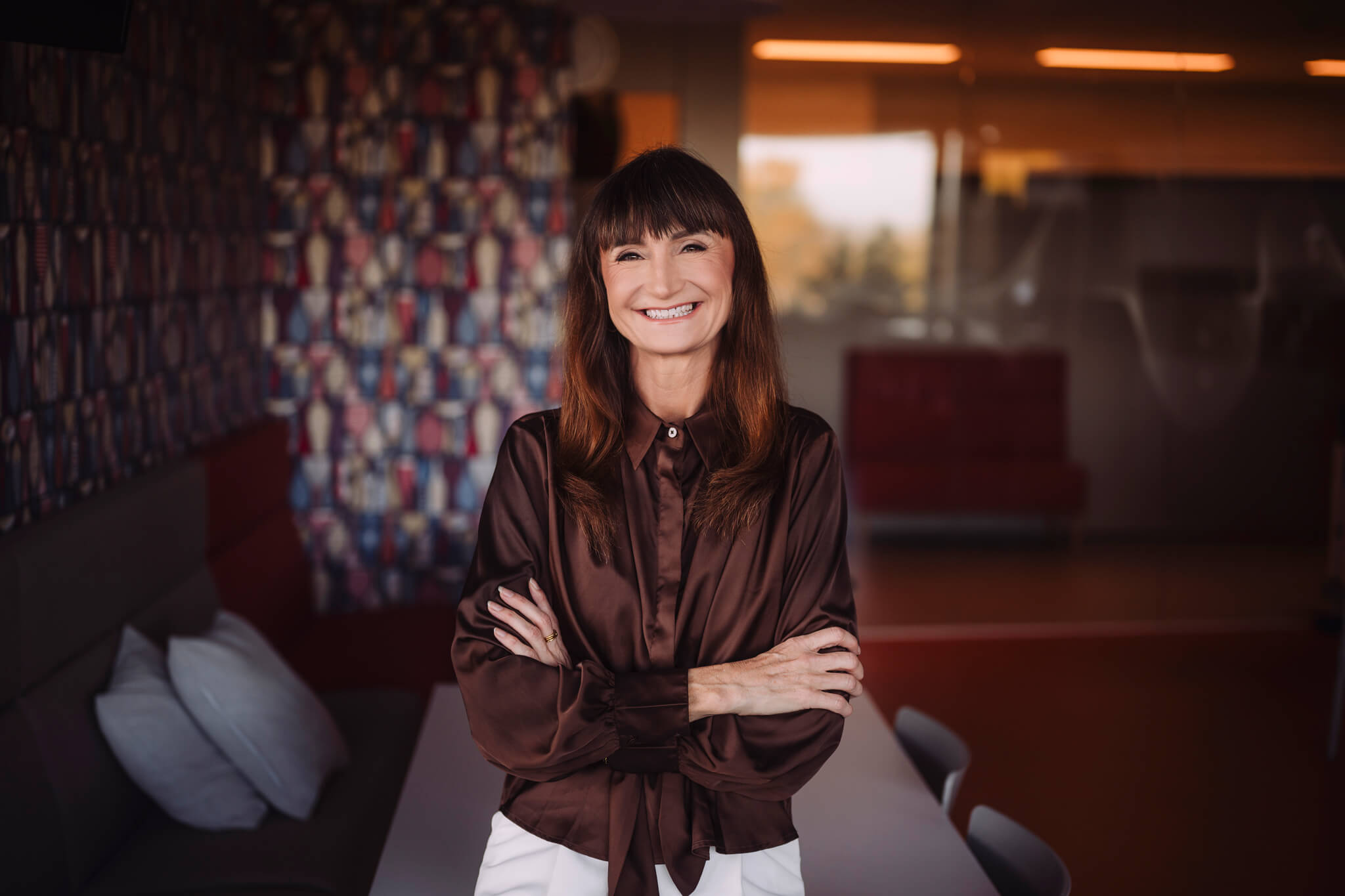 Juhtimiscoach Marika Raiski naeratab, käed ristis, seistes värvikate mustritega kontoriruumis.