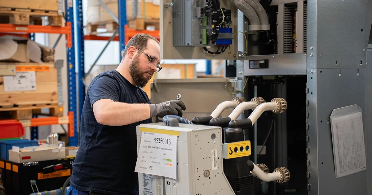 Ein Mitarbeiter von RITTER Starkstromtechnik wartet eine elektrische Schaltanlage in der Produktionshalle. Er prüft und montiert Komponenten an einer geöffneten Mittelspannungsschaltanlage.