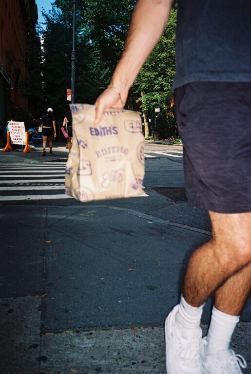 a man walking on the sidewalk holding a bag of bagels from Edith's