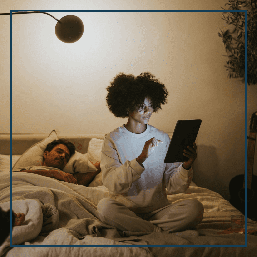 Junge Frau sitzt im Bett und arbeitet an Tablet, Mann schläft