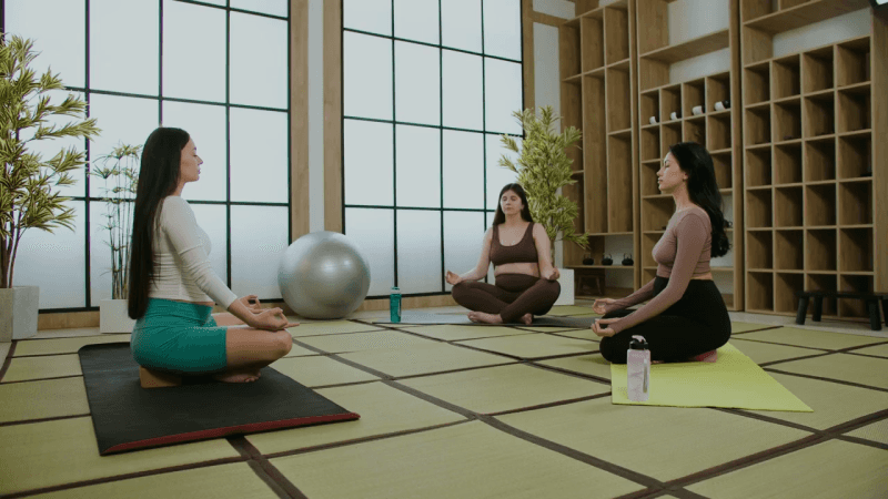 Three women practicing yoga on mats in a serene indoor setting, focusing on their poses and mindfulness.