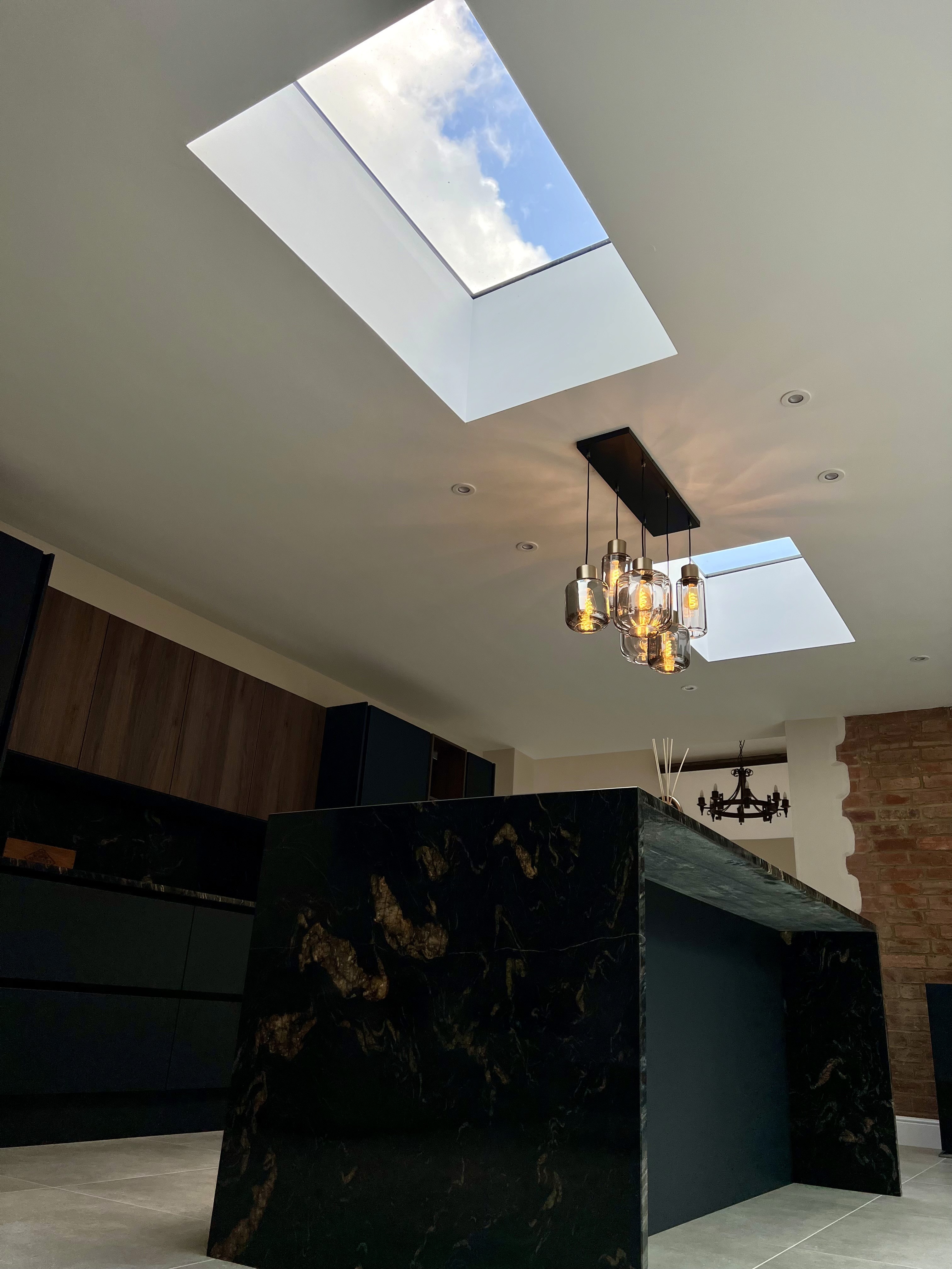 Modern black kitchen renovation with a waterfall marble island and overhead skylights, completed by PPM Builders.