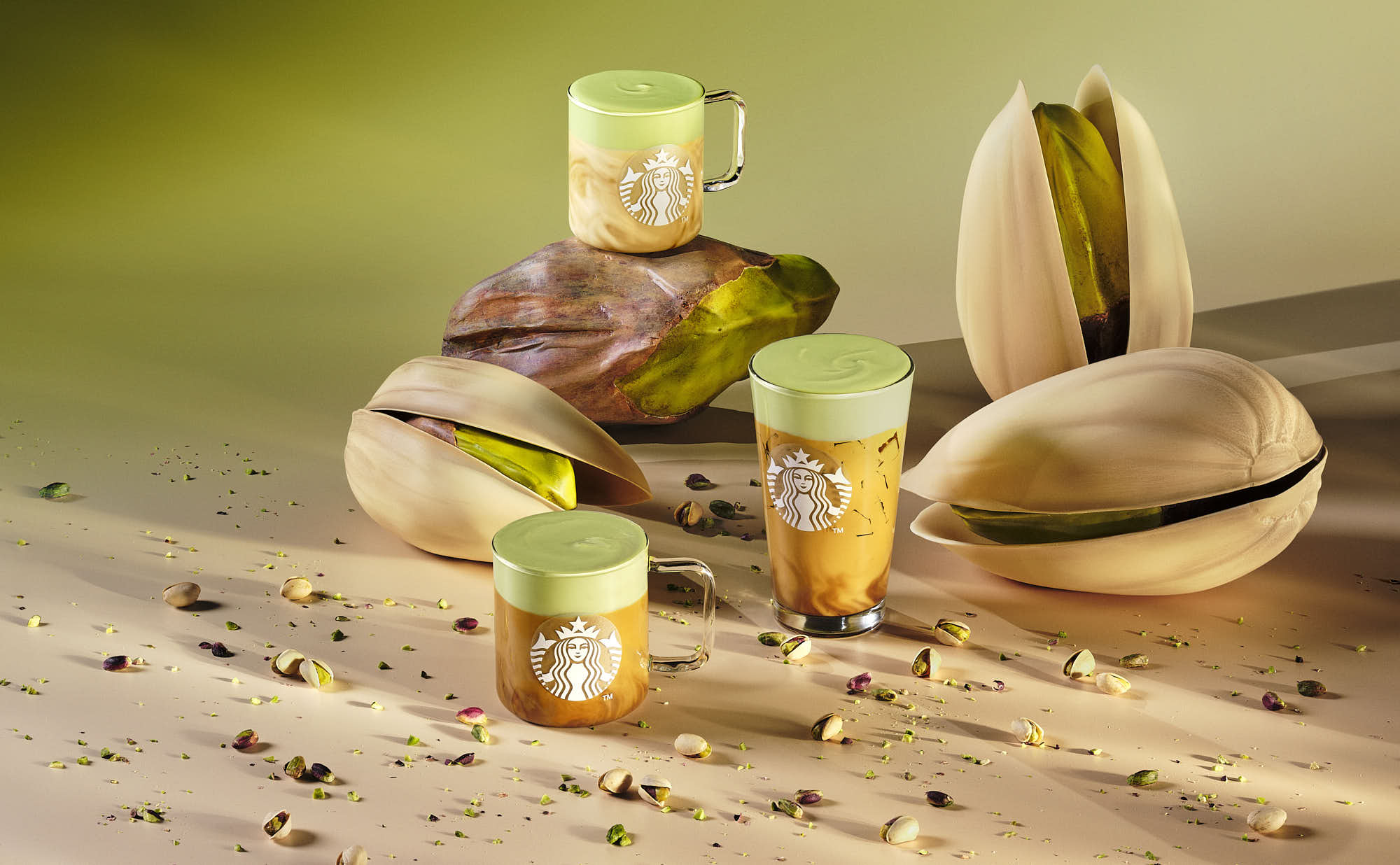 A collection of green pistachio nuts with small glasses of pistachio drinks on a textured surface.