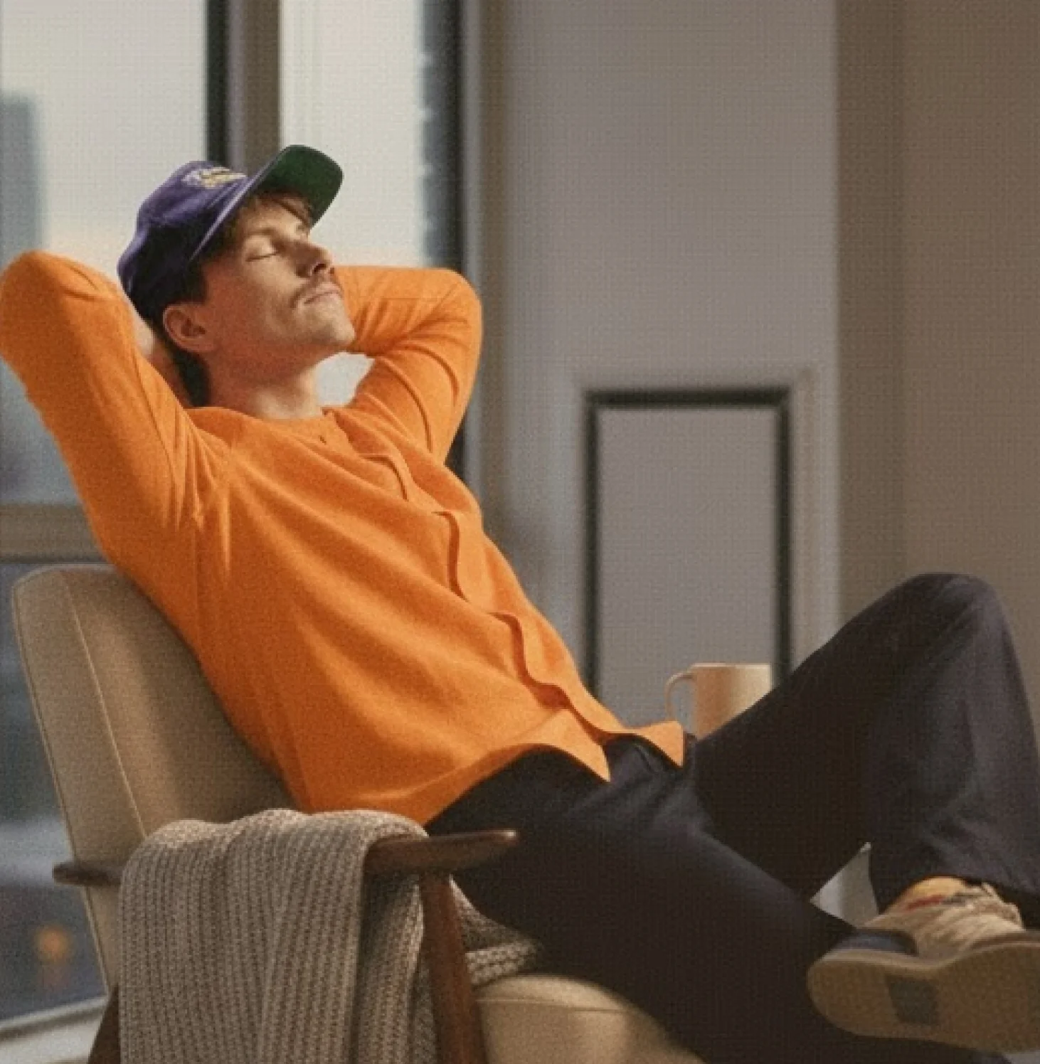 Liam Carter reclining in an armchair by a window in an orange sweater