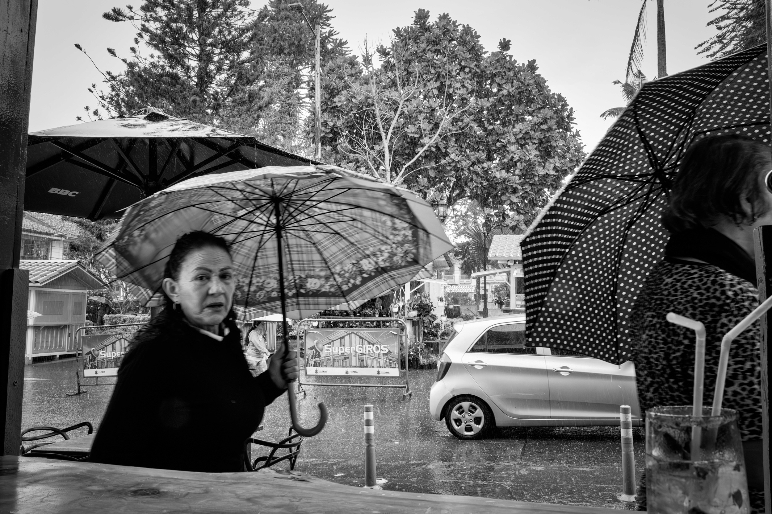 Rainy street scene with people passing by a bar window.