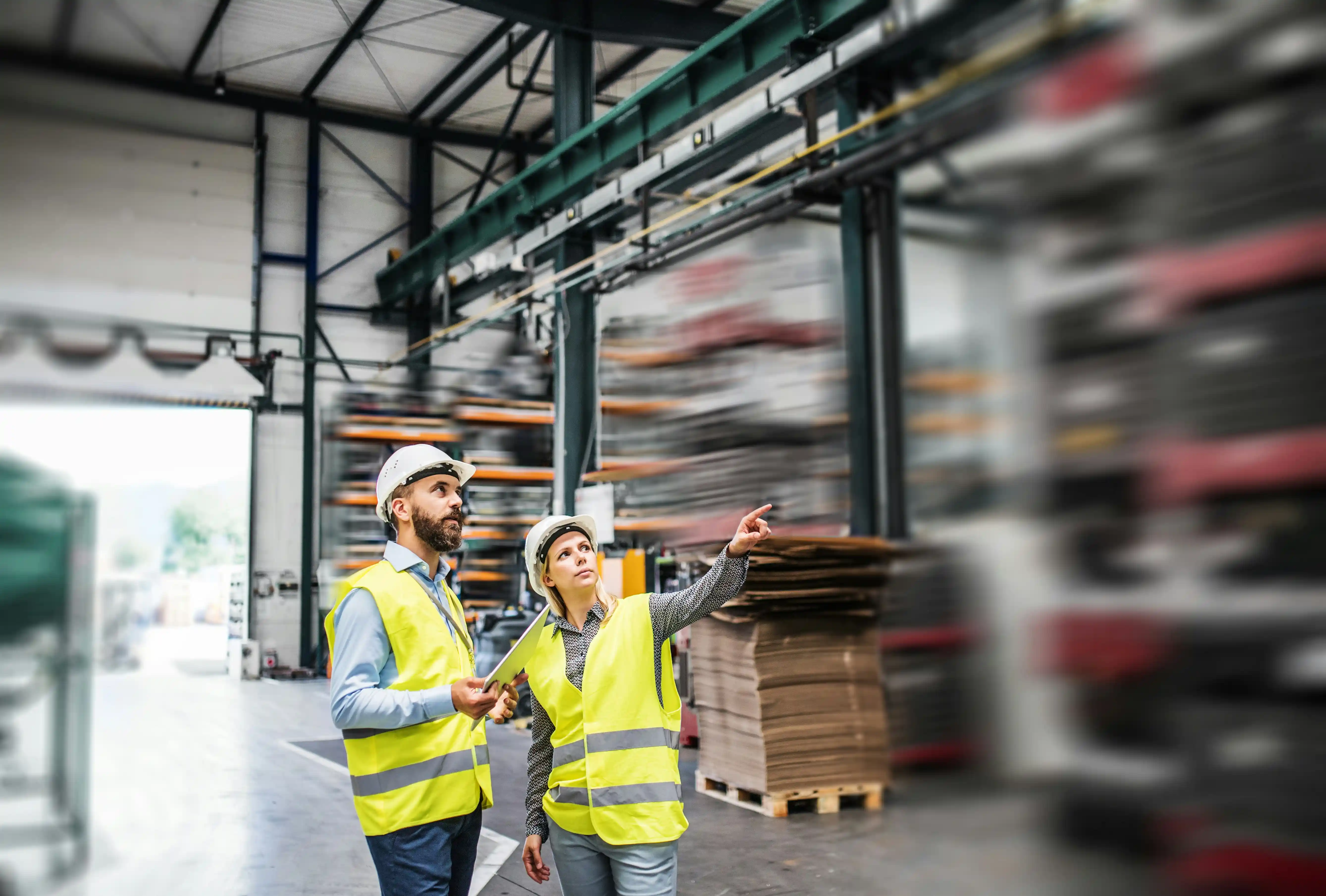 man and woman in high-vis jackets point up at warehouse racking in a 3PL warehouse