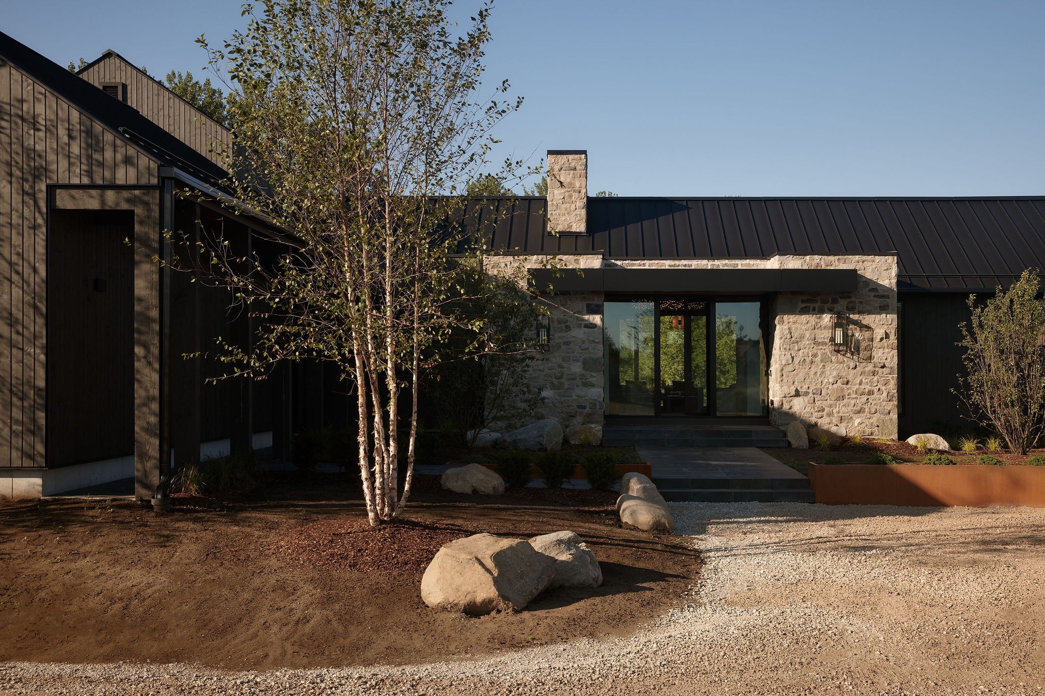 The chalet's stone and timber front, with a birch tree and boulders