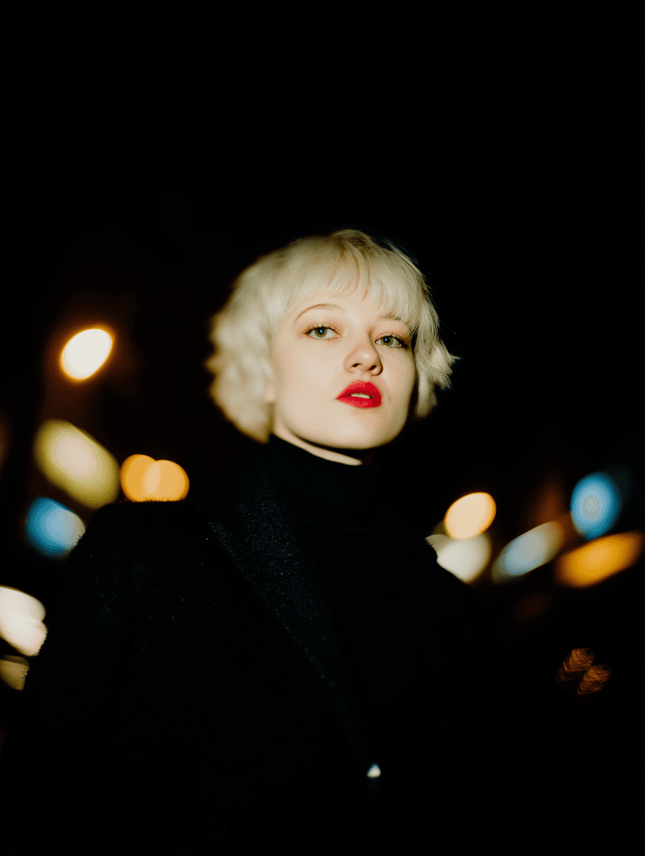 Night portrait of a blonde woman with red lips against urban bokeh lights