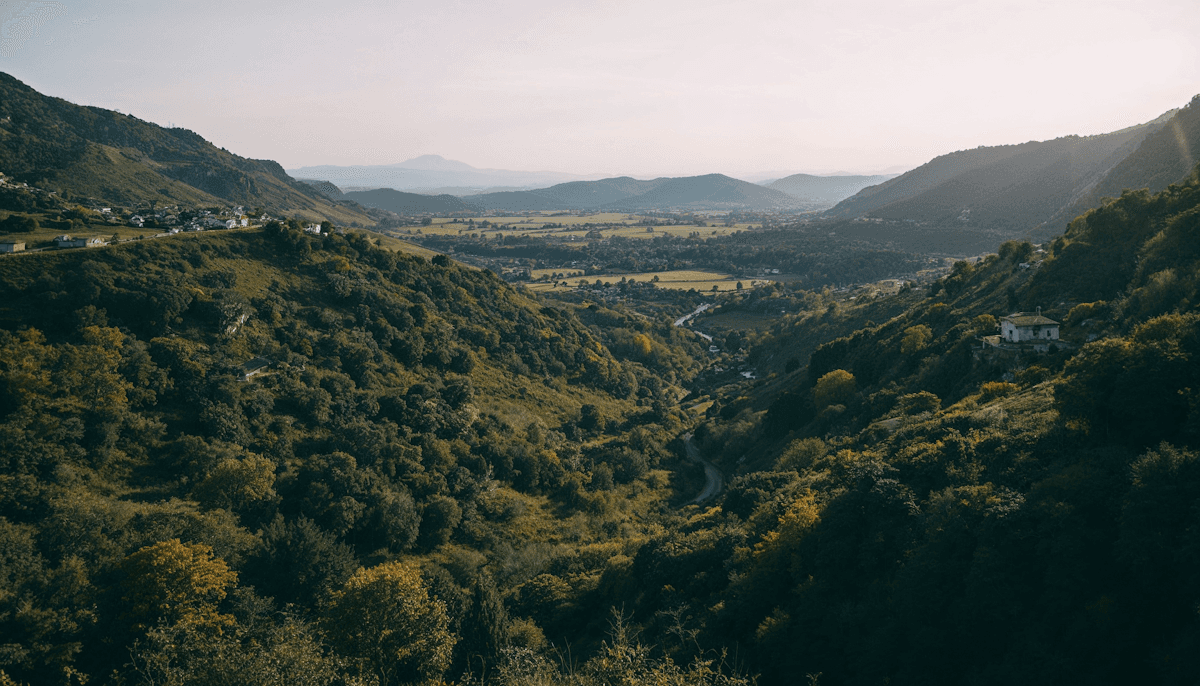 A wooded valley of farmland and scattered hillside houses at dusk