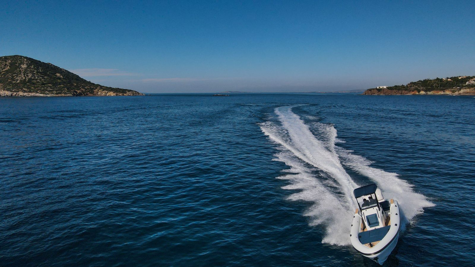 White Rock 36 speedboat with captain at helm cruising calm blue waters near Paros coastline with hills in background.