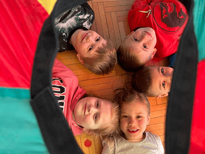 Skupina dětí ležící na zemi v kruhu hlavami k sobě