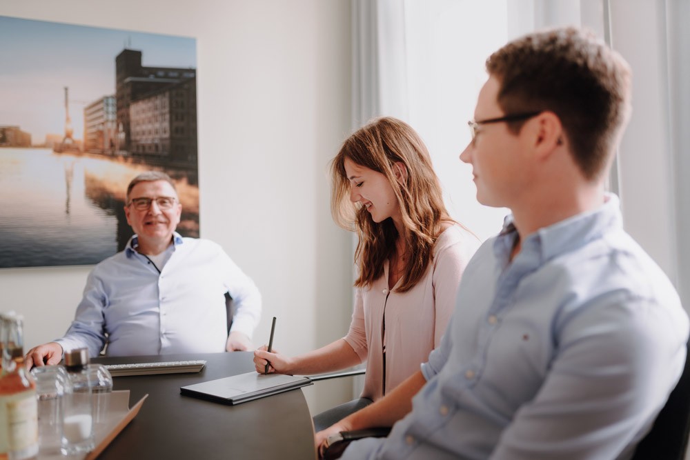 Ein Geschäftsführer und zwei Personen sitzen an einem Konferenztisch und führen ein Gespräch in einem hellen Besprechungsraum von SLB.