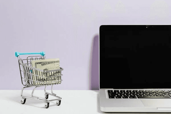 Mini shopping cart with cash beside a laptop.