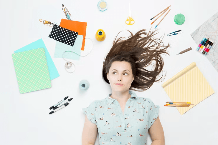 a woman laying on the floor with books, pens, folders, stationaries around her