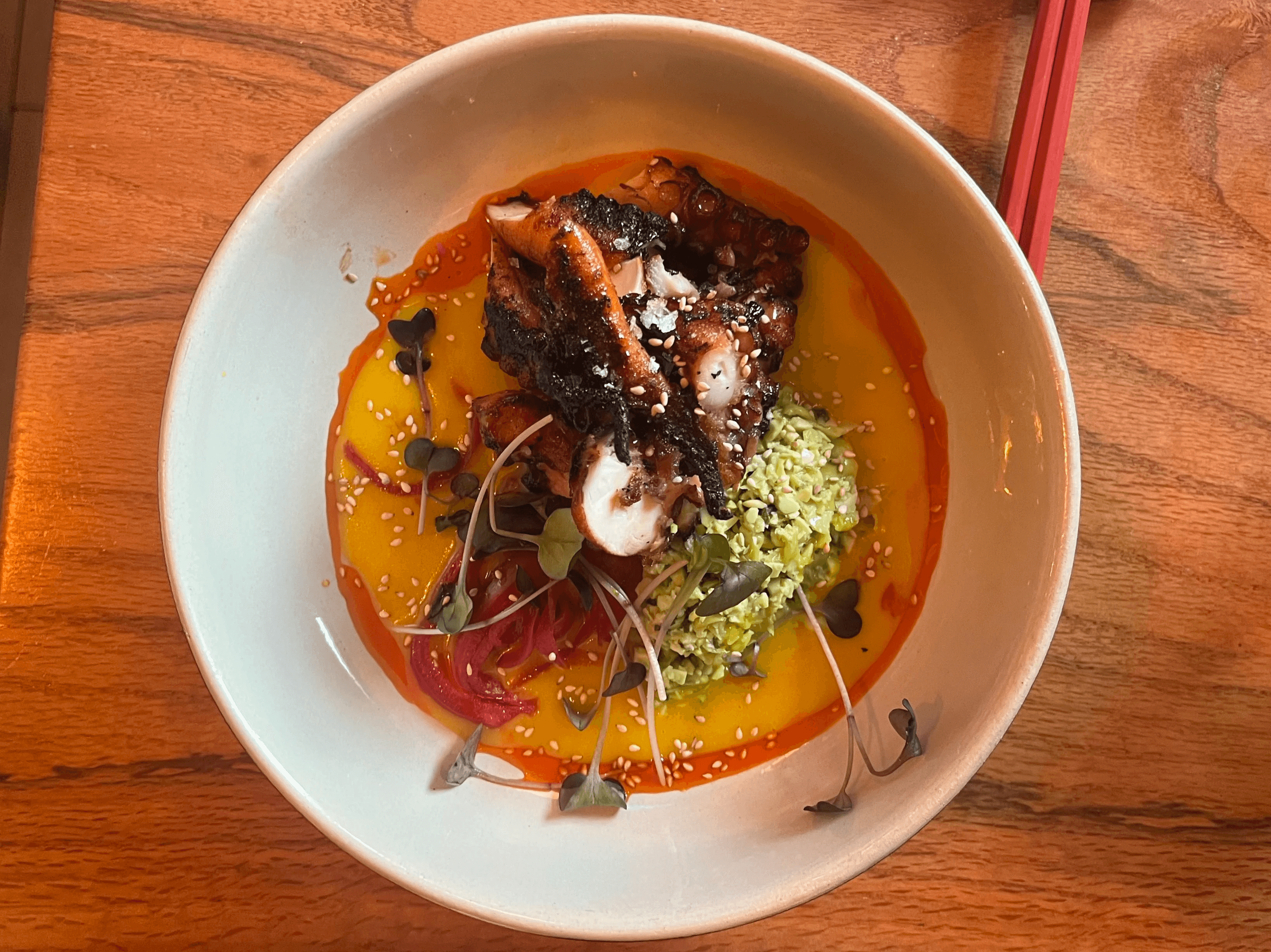 Charred octopus plated with pineapple yuzu glaze and a bed of edamame tabbouleh—an artful fusion dish from 167 Sushi in Charleston.