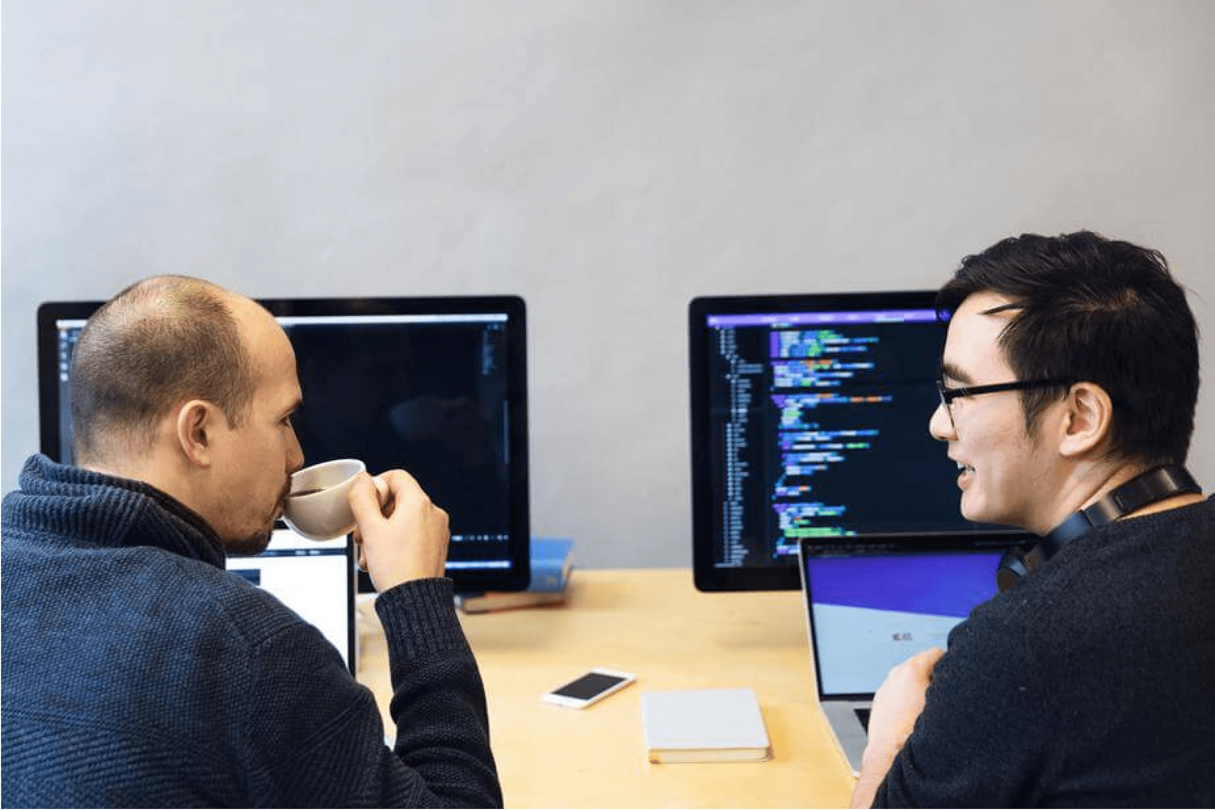Two developers chat while drinking coffee and working at their desks