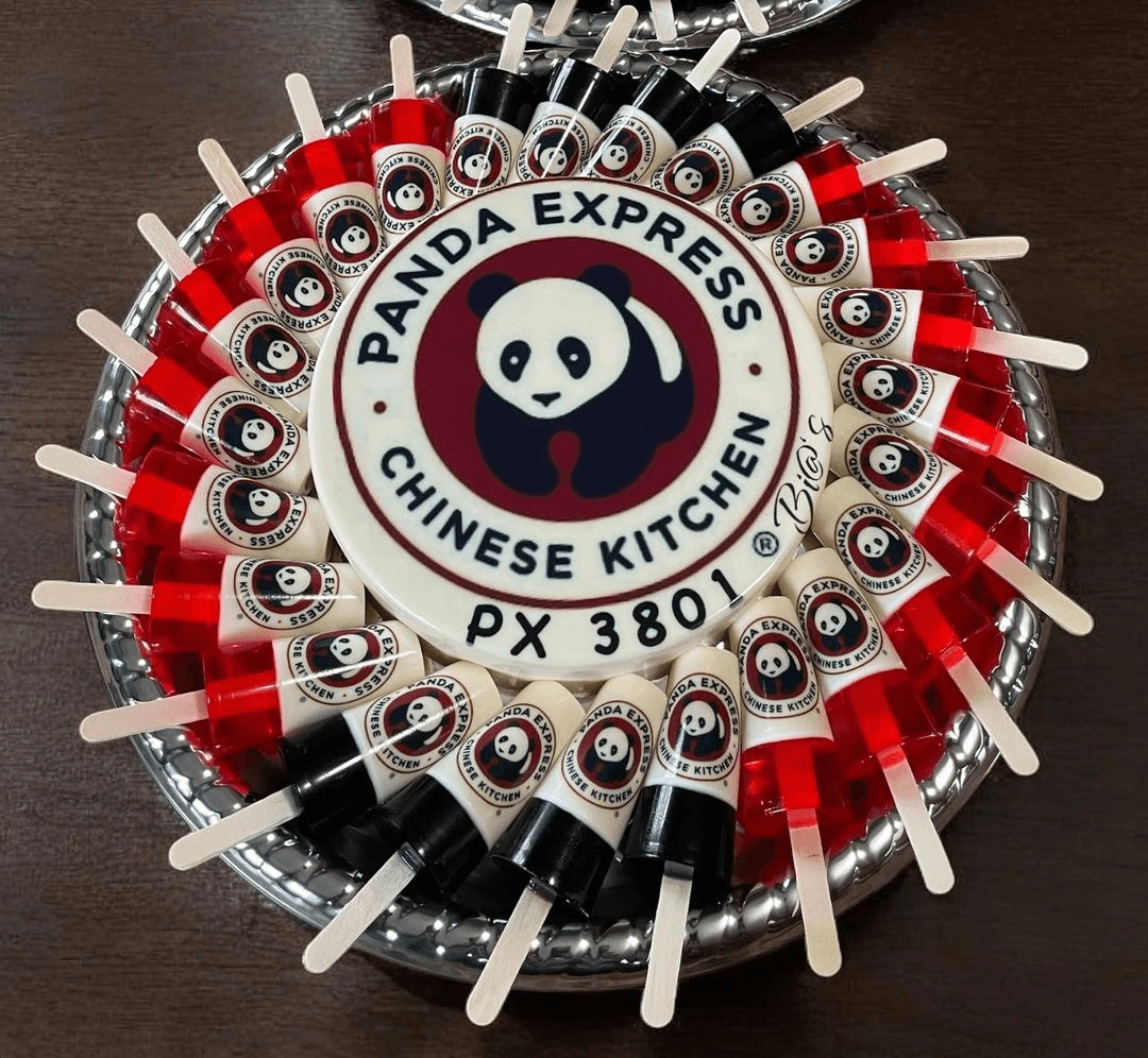 Panda Express-themed gelatin platter with a central cake featuring the iconic panda logo, surrounded by individually decorated gelatin cups in red, white, and black. Ideal for themed events or brand celebrations. Susa’s Sweets & Balloons.