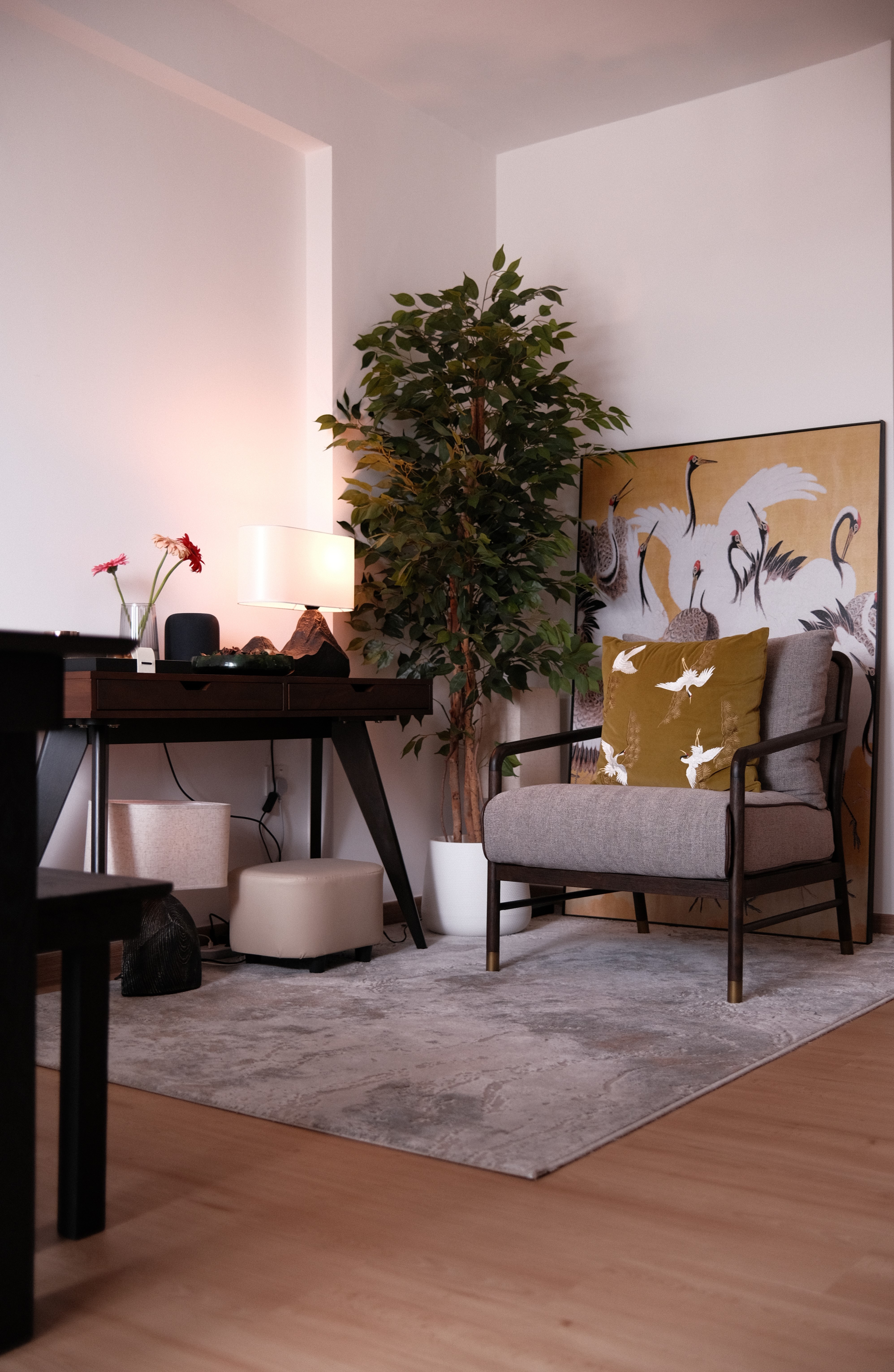 Cozy armchair with mustard crane-print pillow and decorative Asian screen, placed next to a potted plant and a terracotta door, in a modern living space.