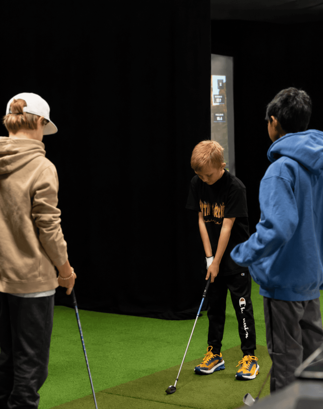 Monitors with golf simulations and golf bags next to a simulated green at an indoor facility.