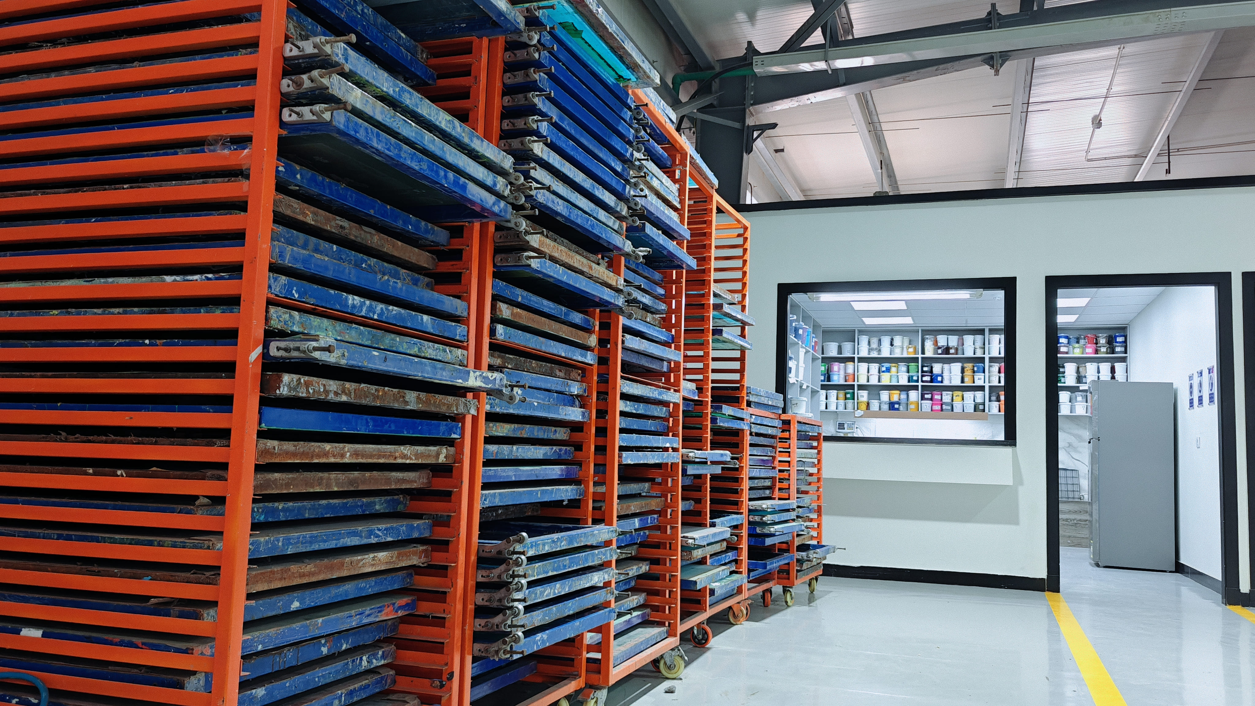 Screen printing workshop showing organized drying racks with multiple printing frames.